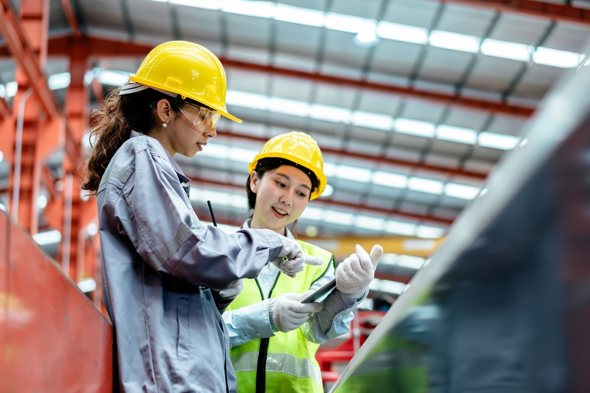 Two women are working in a factory and looking at a tablet.