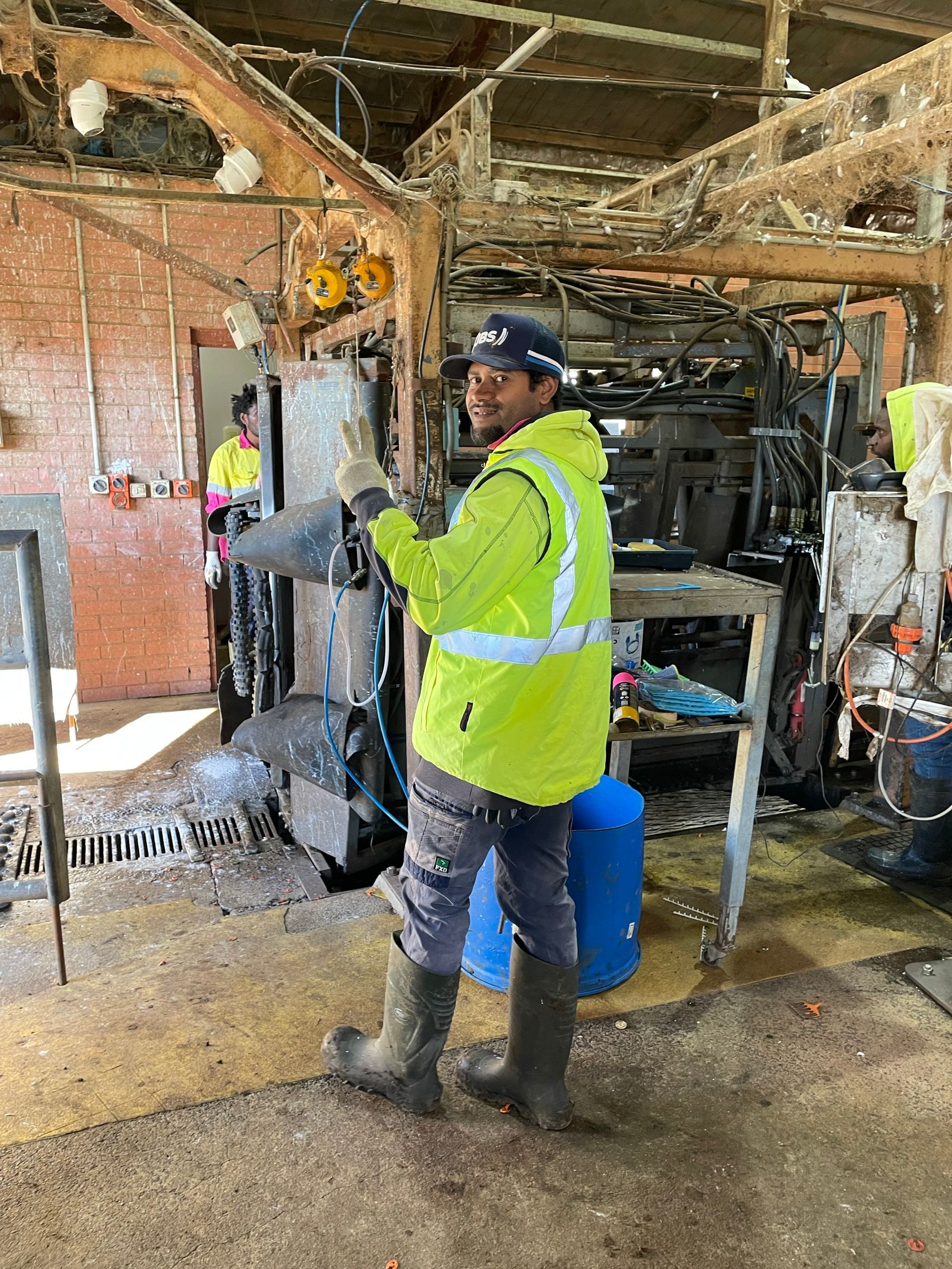 A man in a yellow vest is standing in a barn holding a machine.