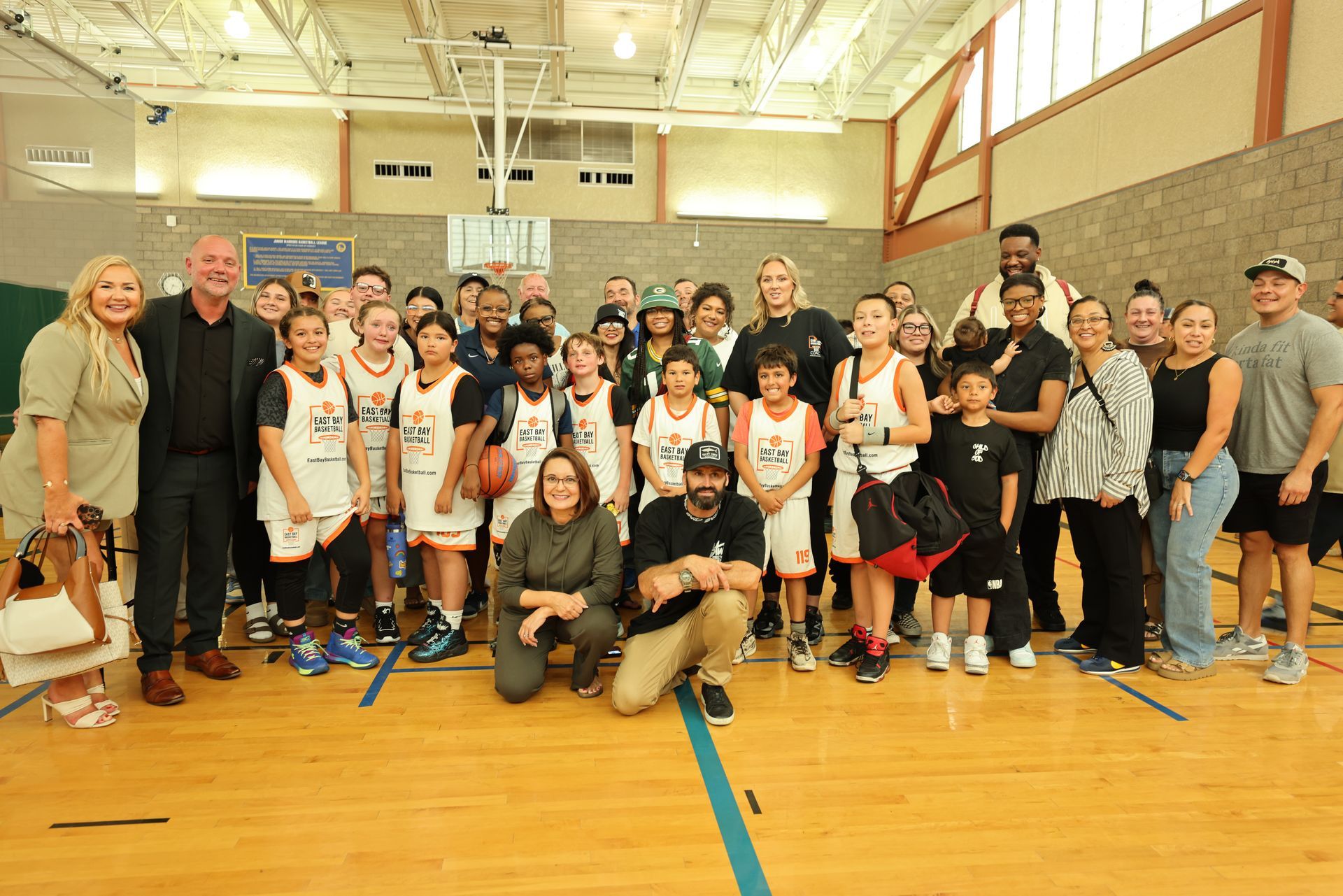 A group of children in basketball jerseys and adults pose together on a basketball court.