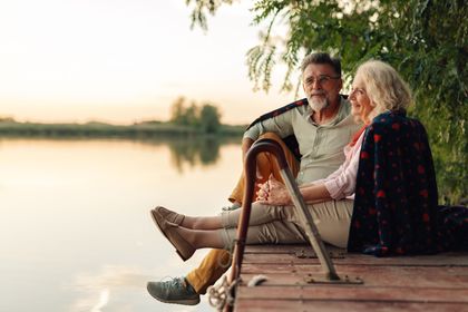 Two people sit on a wooden dock by a calm lake at sunset, relaxing and talking. Two people sit on a wooden dock by a calm lake at sunset, relaxing and talking.