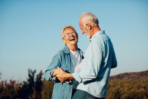Two people laughing and holding hands in a sunlit field under a clear blue sky Two people laughing and holding hands in a sunlit field under a clear blue sky