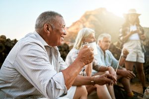 Friends sitting outdoors at sunset, sharing drinks and conversation on a campsite or patio. Friends sitting outdoors at sunset, sharing drinks and conversation on a campsite or patio.