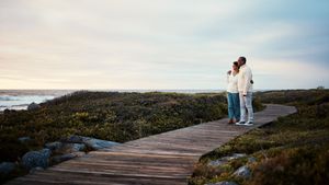 Two people standing on a wooden boardwalk by the sea at sunset Two people standing on a wooden boardwalk by the sea at sunset