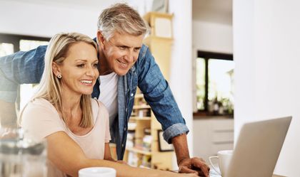 Two people smiling at a laptop in a bright home kitchen Two people smiling at a laptop in a bright home kitchen