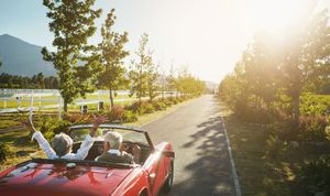 Red convertible driving on a sunny country road, with white flowers and trees along the fence. Red convertible driving on a sunny country road, with white flowers and trees along the fence.