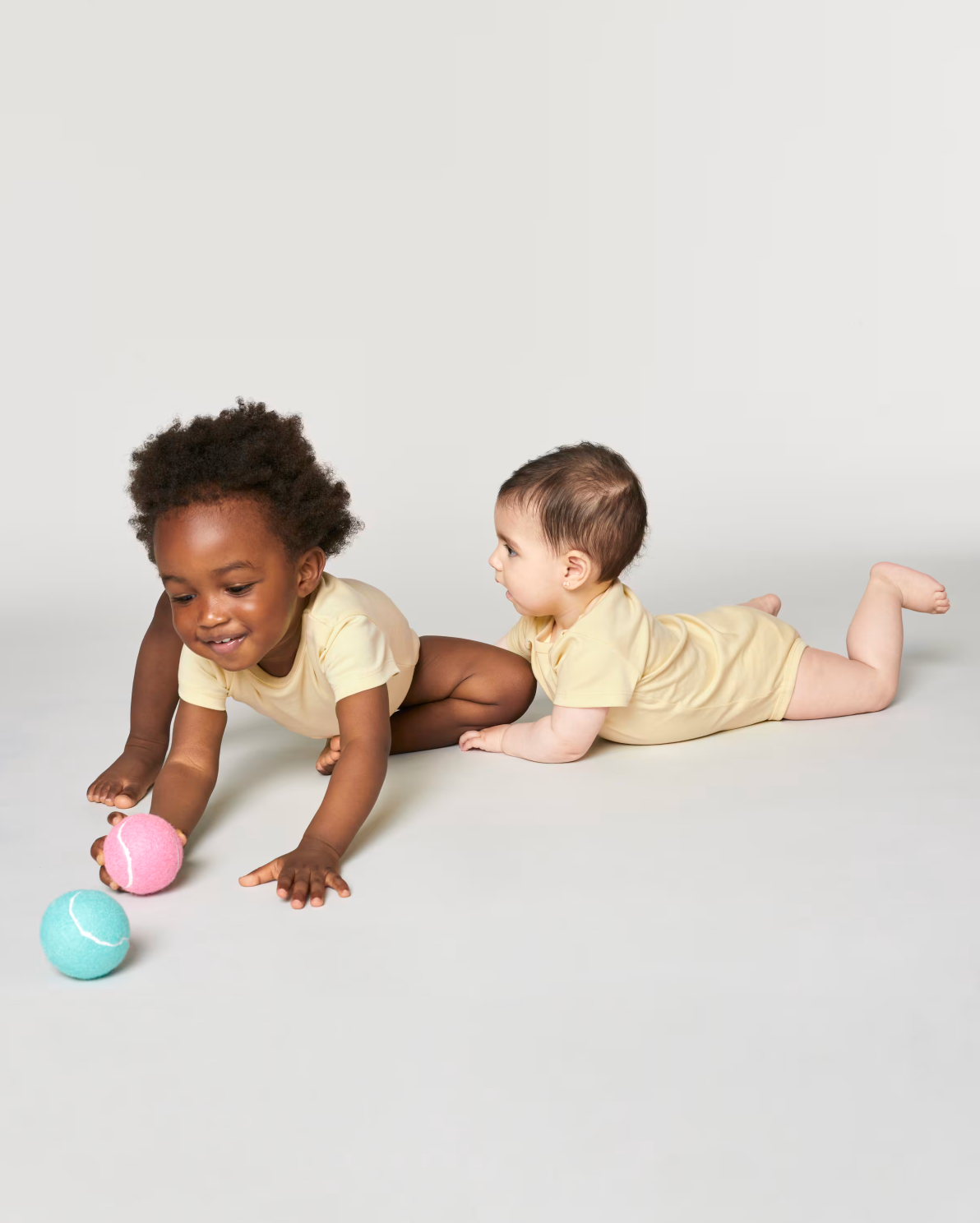 Twee baby's in een licht geel rompertje van biologisch katoen, een origineel kraamcadeau van Taadaa
