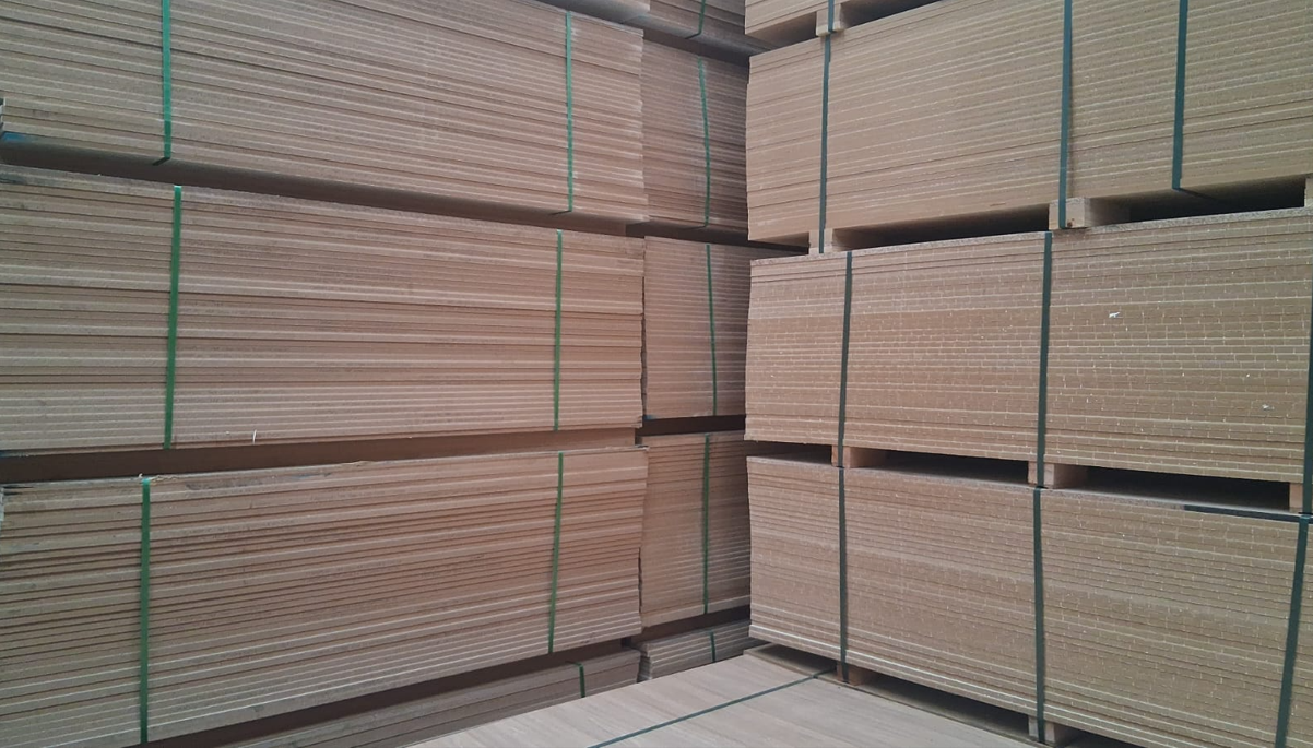 Montones de láminas de cartón beige atadas con correas verdes en un área de almacenamiento de un almacén.