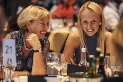 Two women are sitting at a table with wine glasses and smiling.