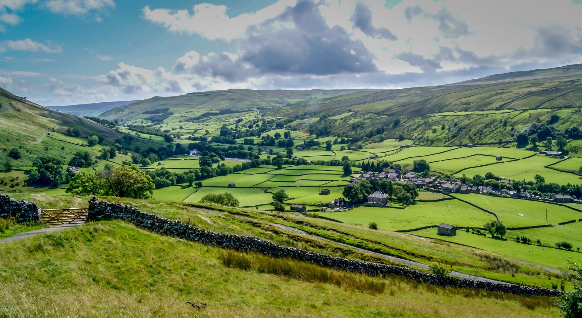 A view of a lush green valley with a stone wall in the foreground.