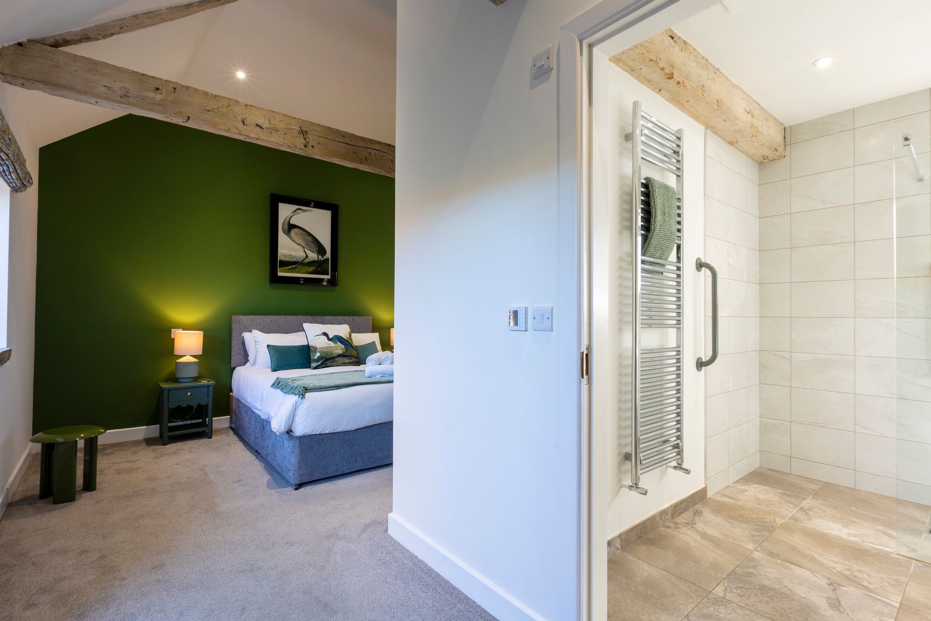 Bedroom with green accent wall, bed, and ensuite shower room with heated towel rack.