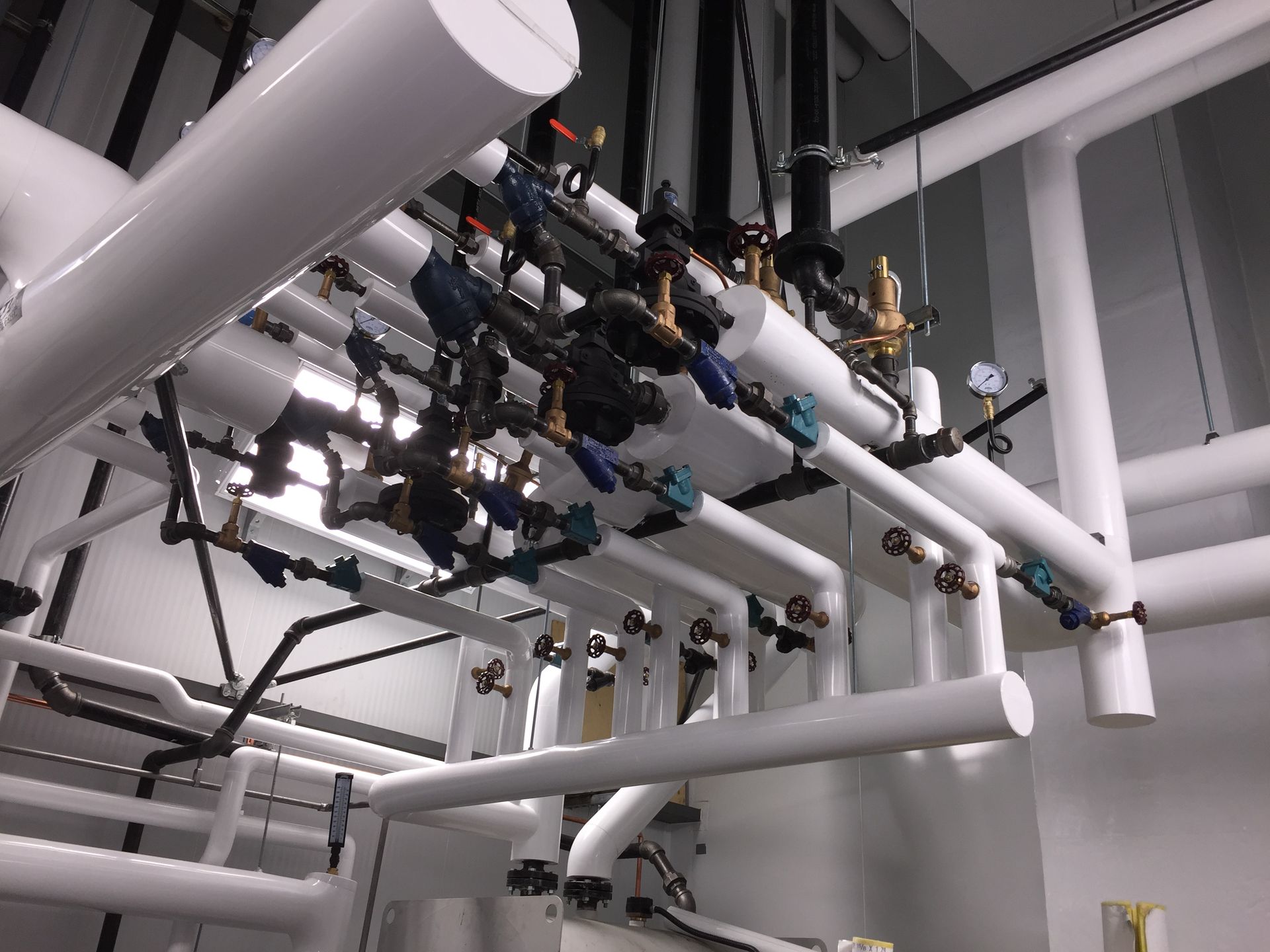 Tuyaux et vannes industriels au plafond d'un local technique, avec tuyauterie blanche et noire au plafond.
