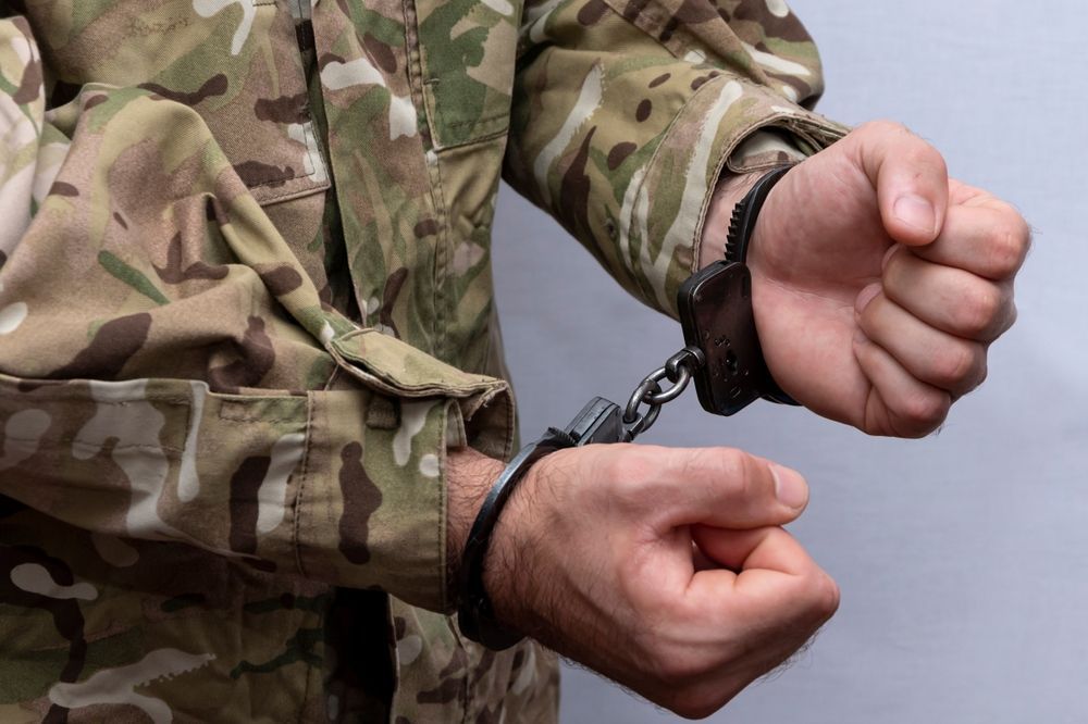 A soldier in a camouflage uniform is handcuffed.