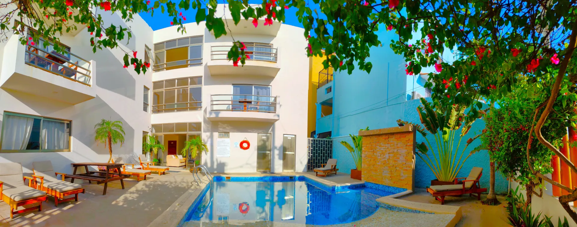 Un complejo tropical con piscina, edificios blancos y exuberante vegetación bajo un cielo azul brillante.