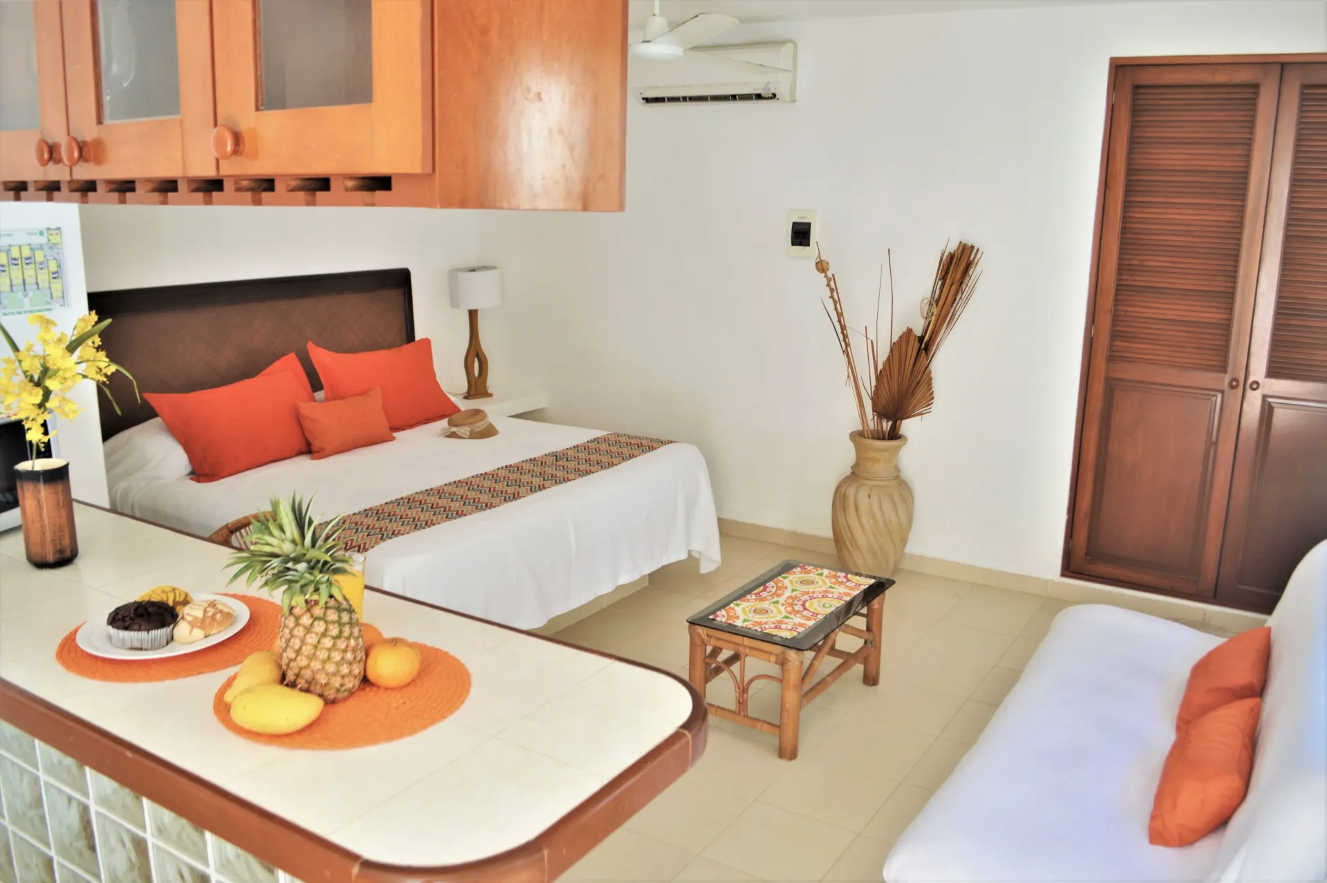 Pequeño monoambiente en tonos naranjas y neutros, incluye cama, fruta y sofá.
