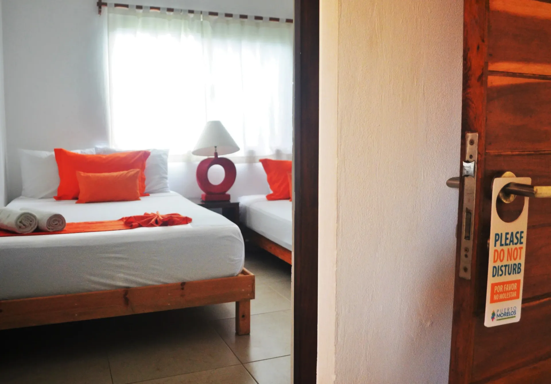 Dos camas individuales con detalles en naranja en una habitación luminosa, vista a través de una puerta .