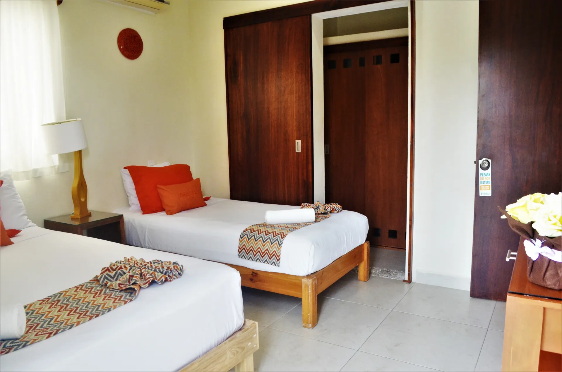Dormitorio con dos camas individuales, muebles de madera y almohadas y decoración con detalles en color naranja.