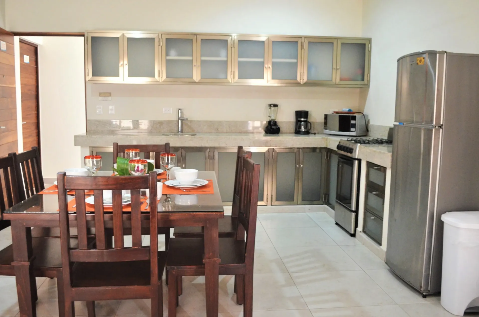 Kitchen with stainless steel cabinets, appliances, wooden dining table with place settings.