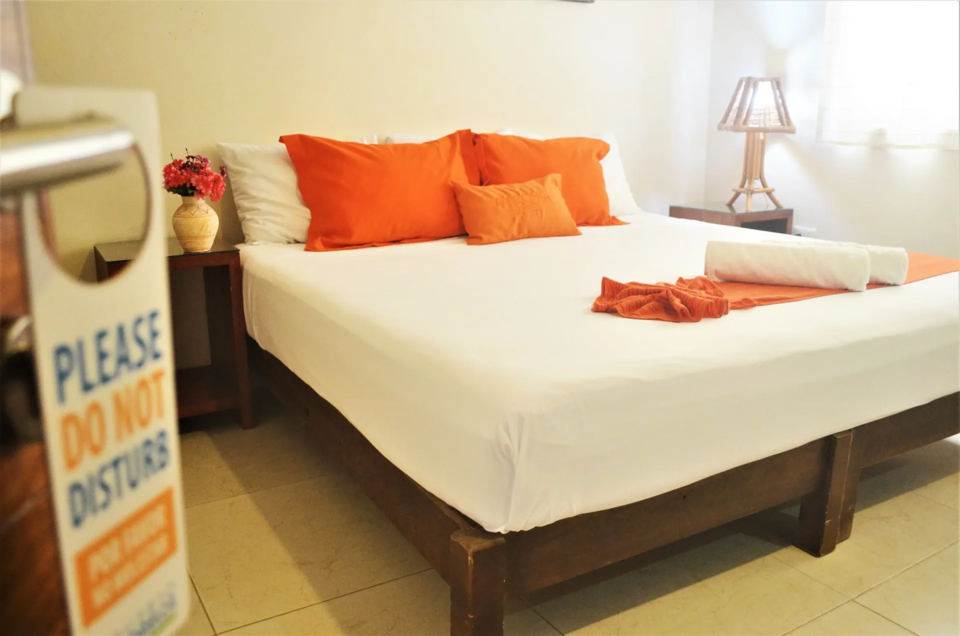 Dormitorio con cama de matrimonio, sábanas blancas, almohadas naranjas y cartel de 