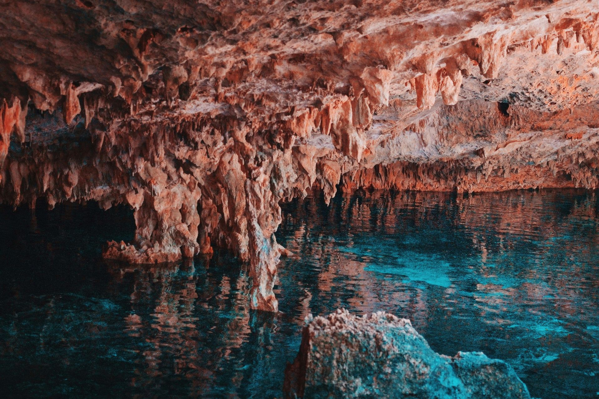 Cave interior with stalactites reflected in turquoise water.