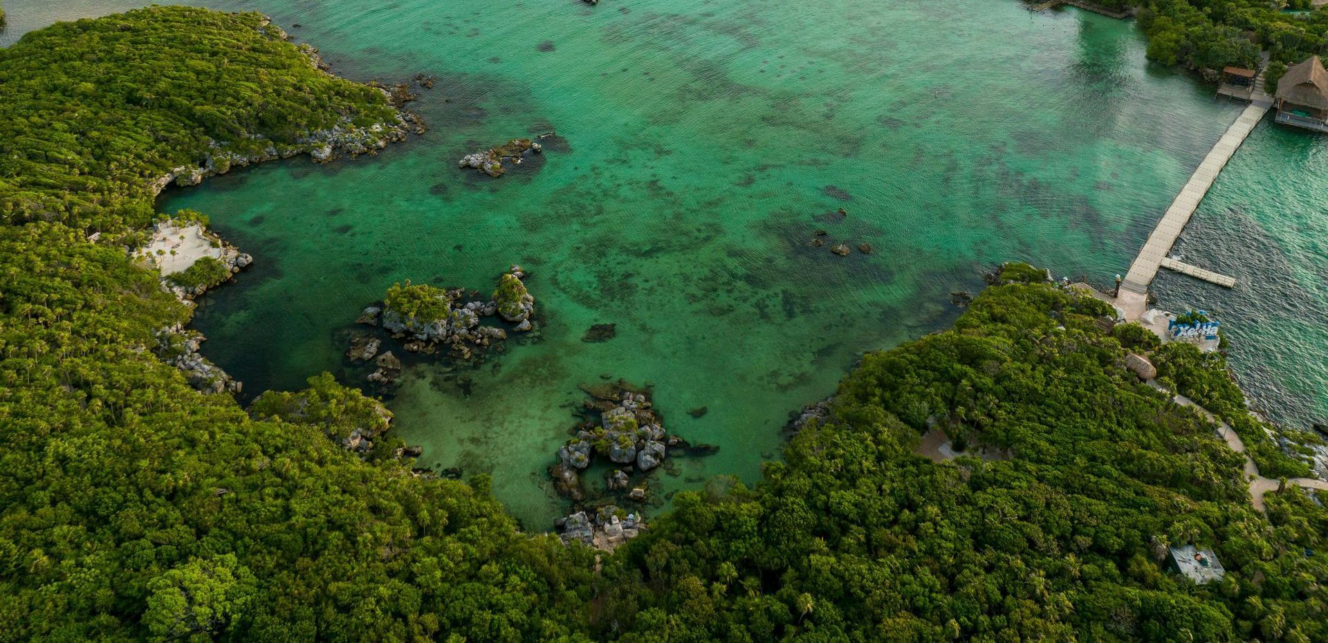 Aerial view of a tropical lagoon surrounded by lush green foliage. Clear turquoise water. Pier extending into the lagoon.