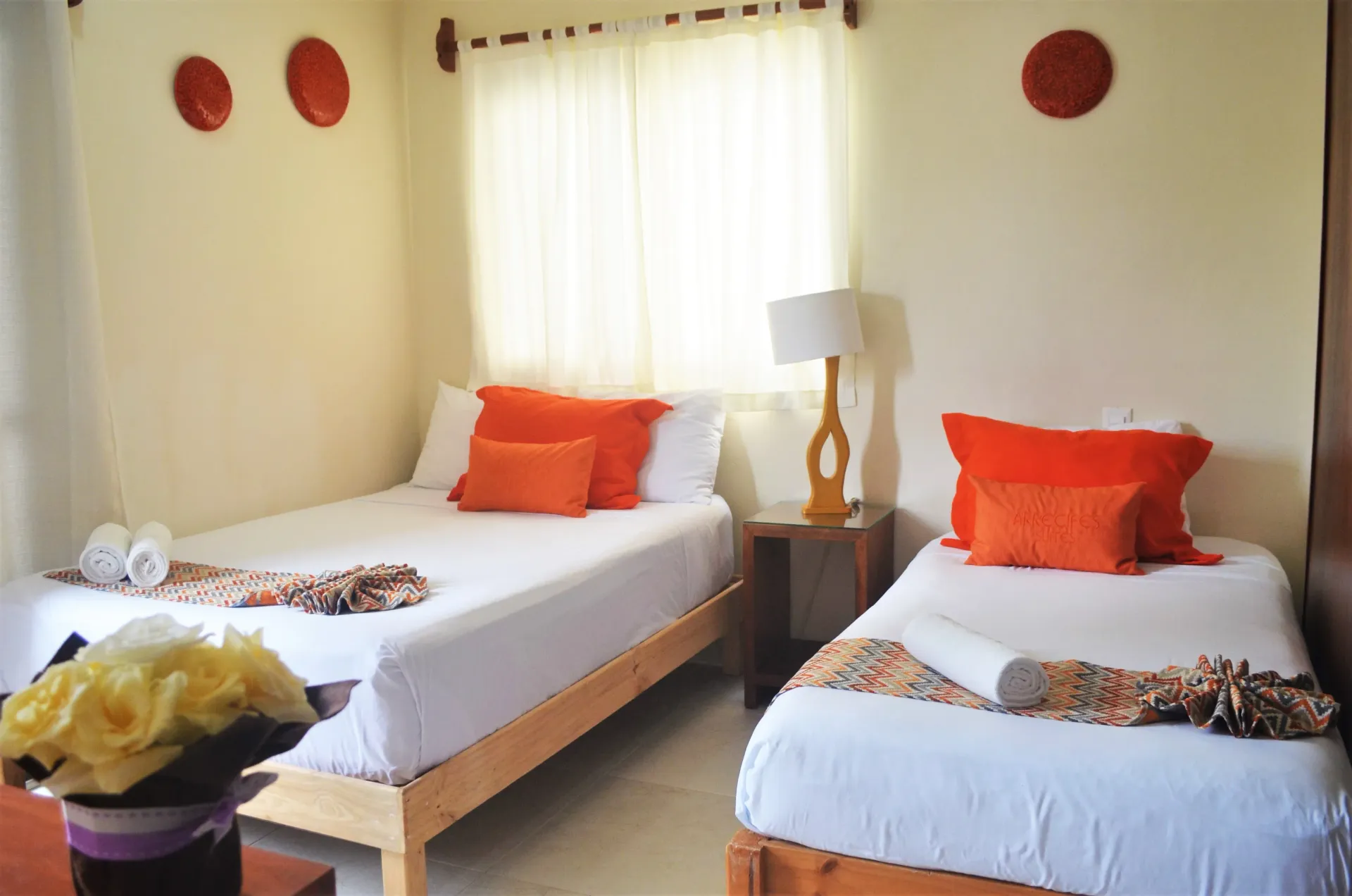 Dormitorio con dos camas individuales, ropa de cama blanca, almohadas naranjas, detalles de madera .