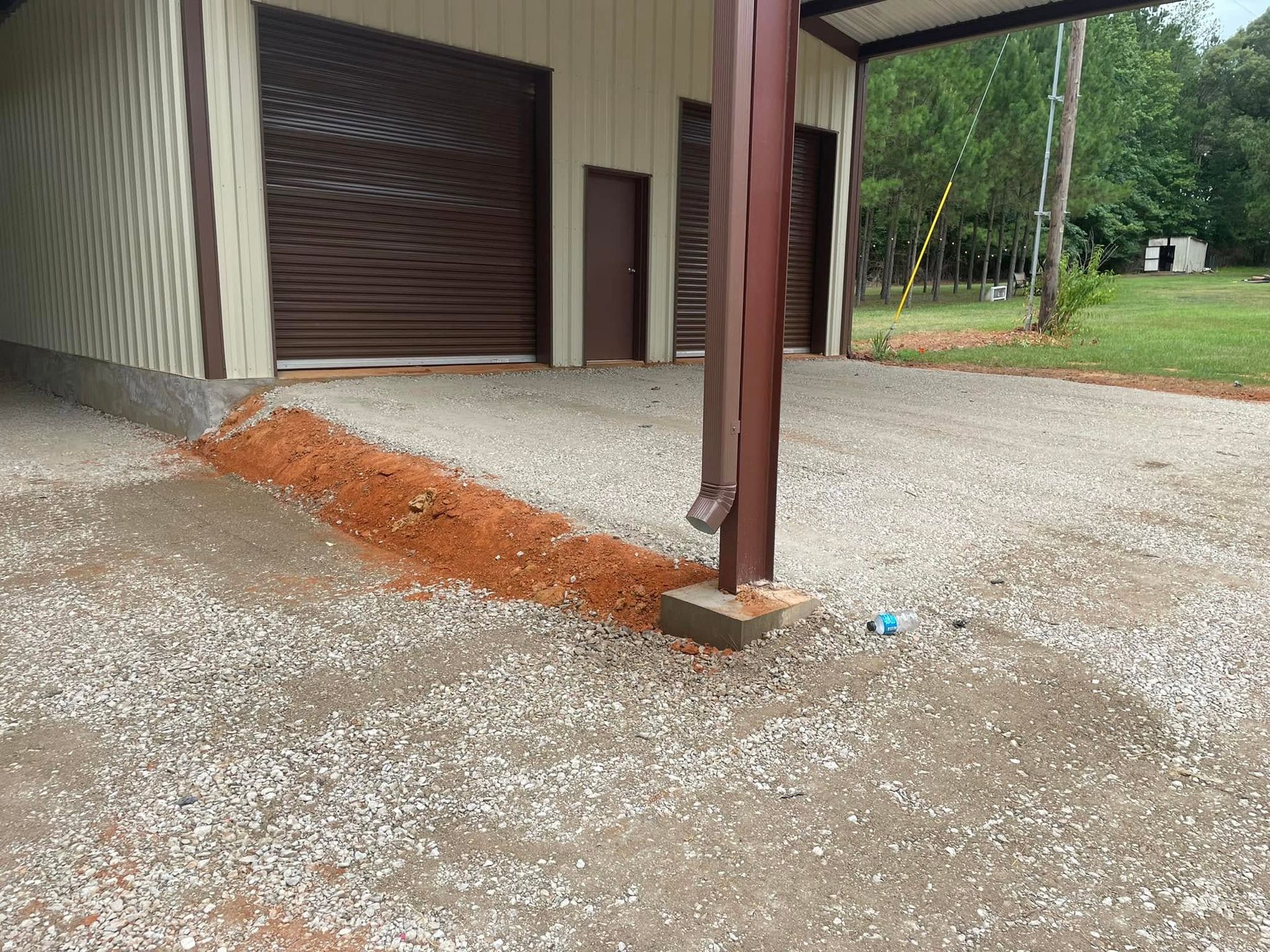 Carport with gravel driveway and an orange dirt slope beside a garage and support post