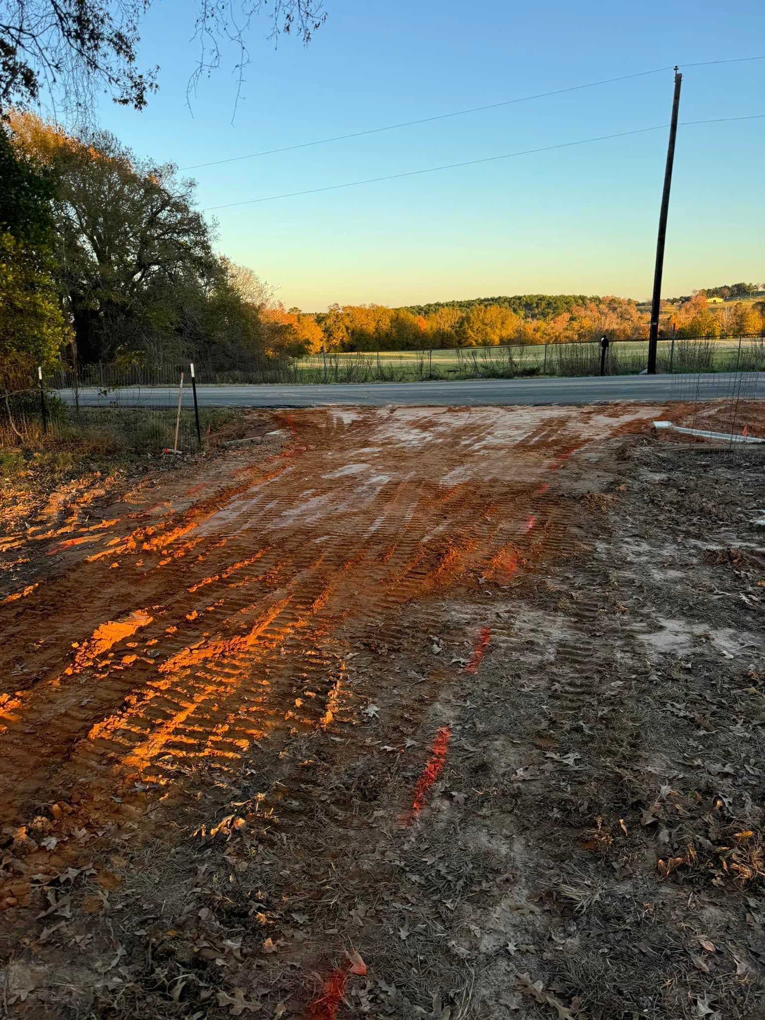 Dirt road at sunset beside a lake, with orange light on the ground and trees lining the shore.