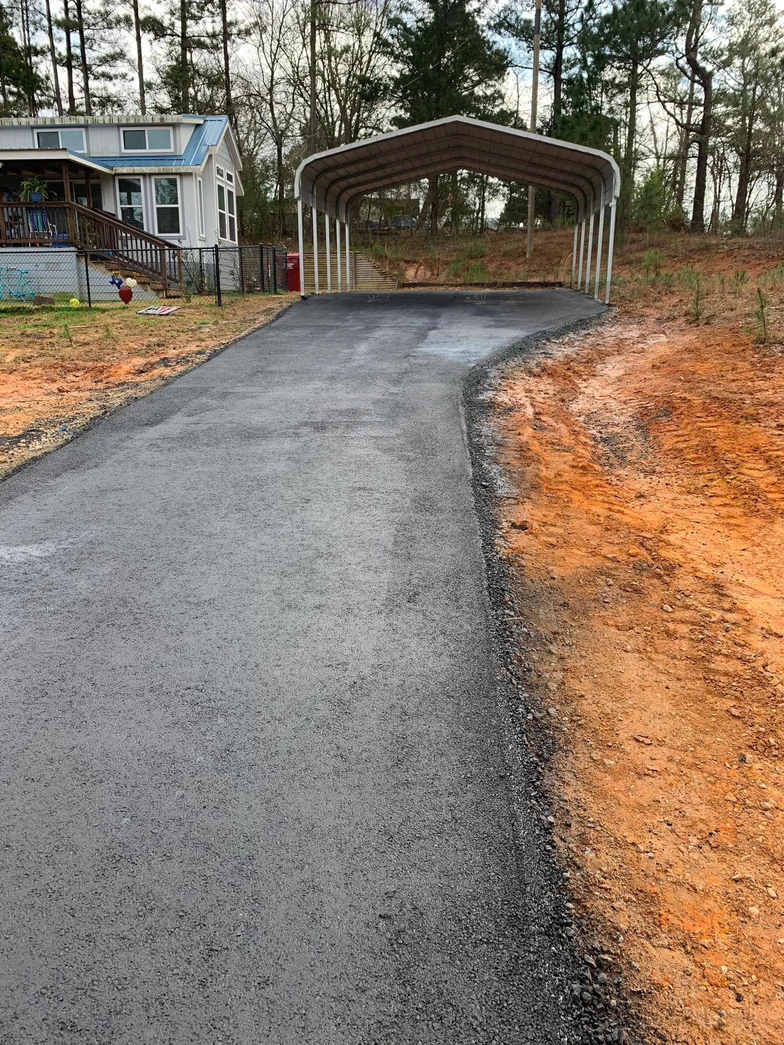 Wet driveway leading to a covered carport beside a house in a wooded yard