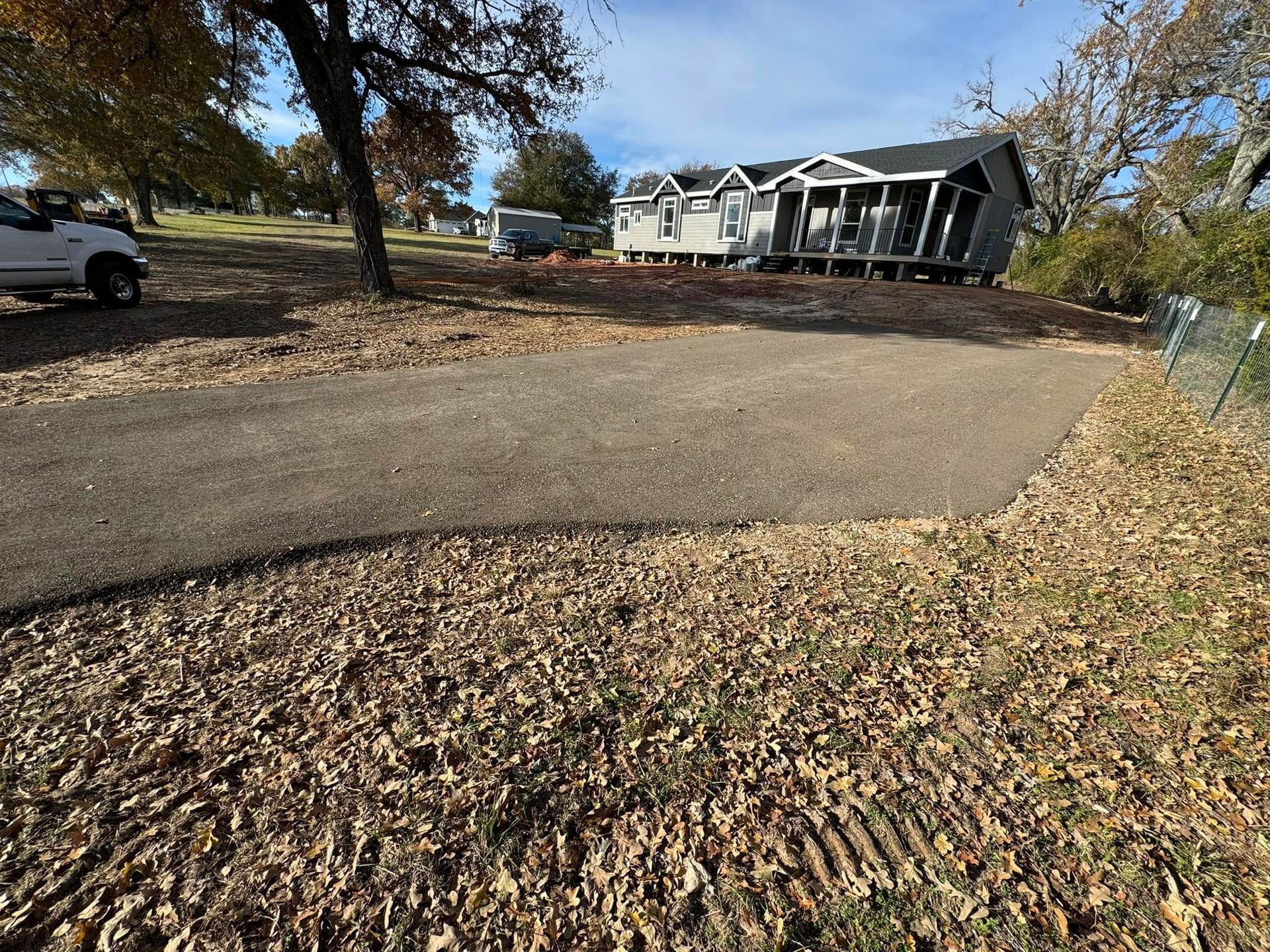 Curving driveway in front of a house, covered with fallen autumn leaves and trees on both sides.
