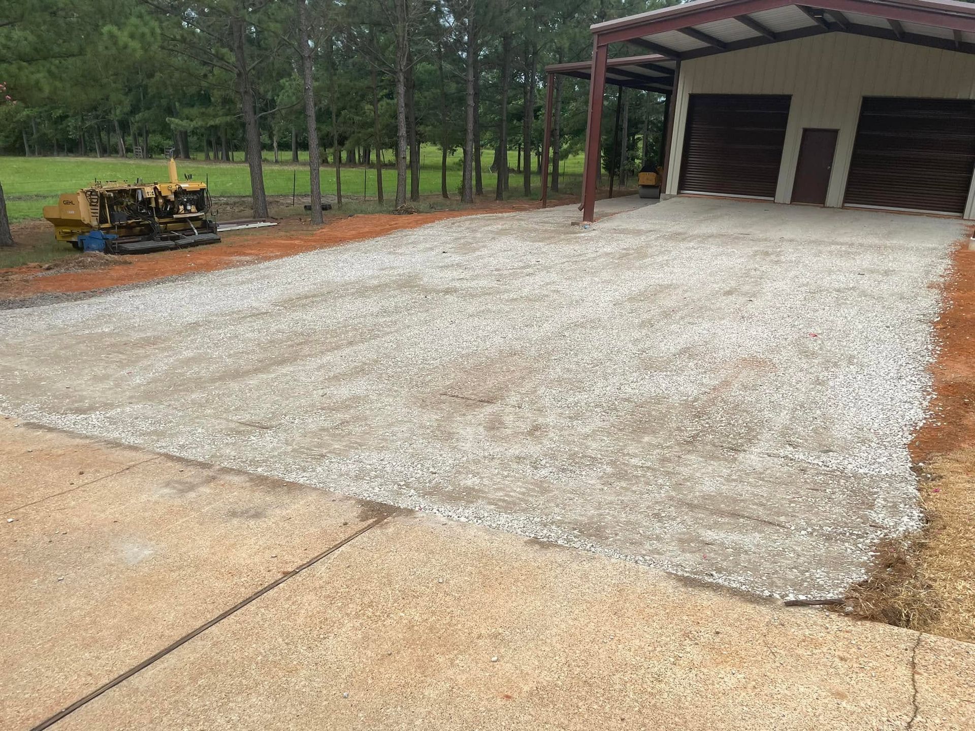 Gravel driveway beside a garage, with a small bulldozer and trees in the background.