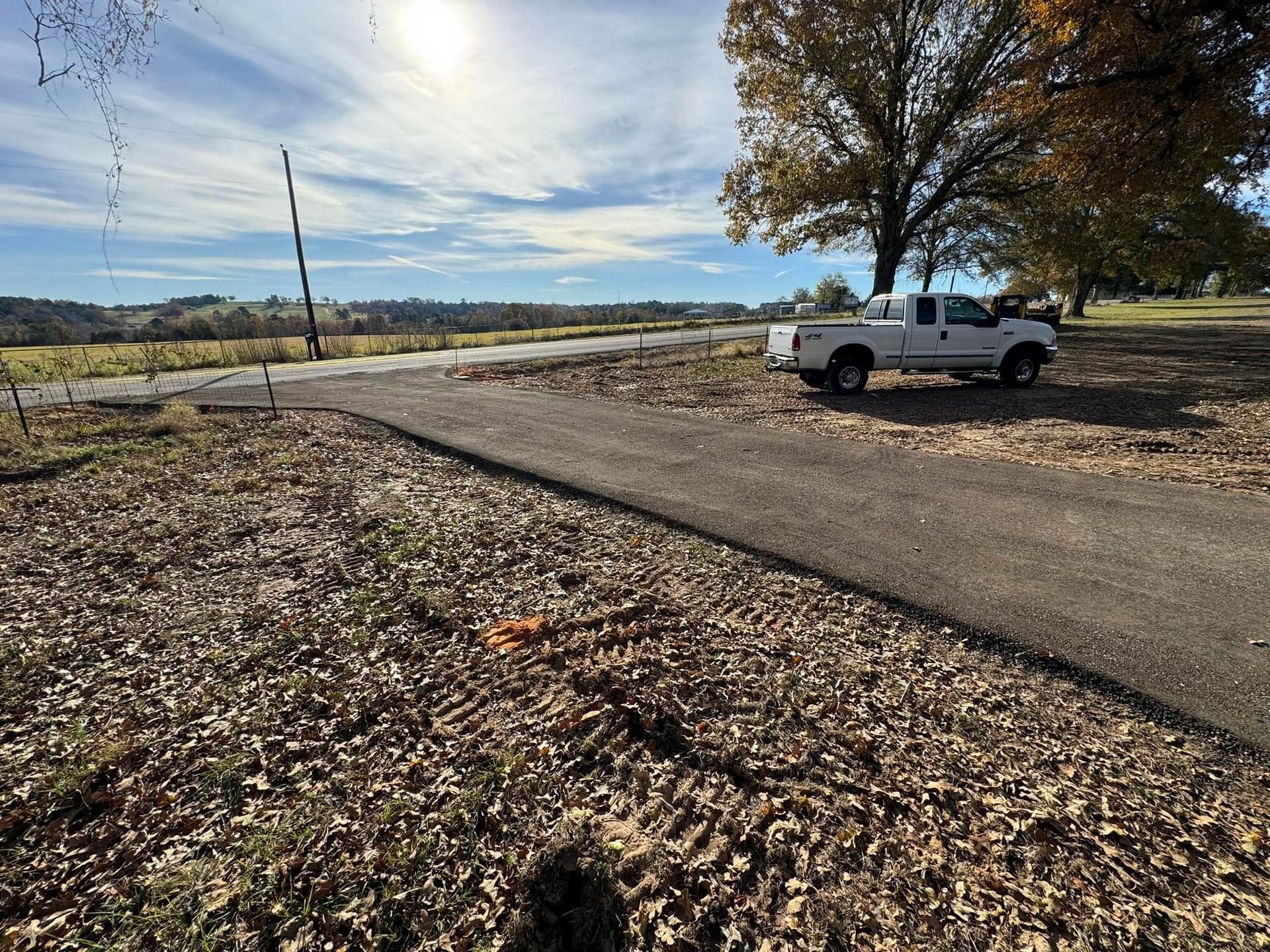 White pickup truck parked on a rural gravel road beside a tree and open fields under a cloudy sky