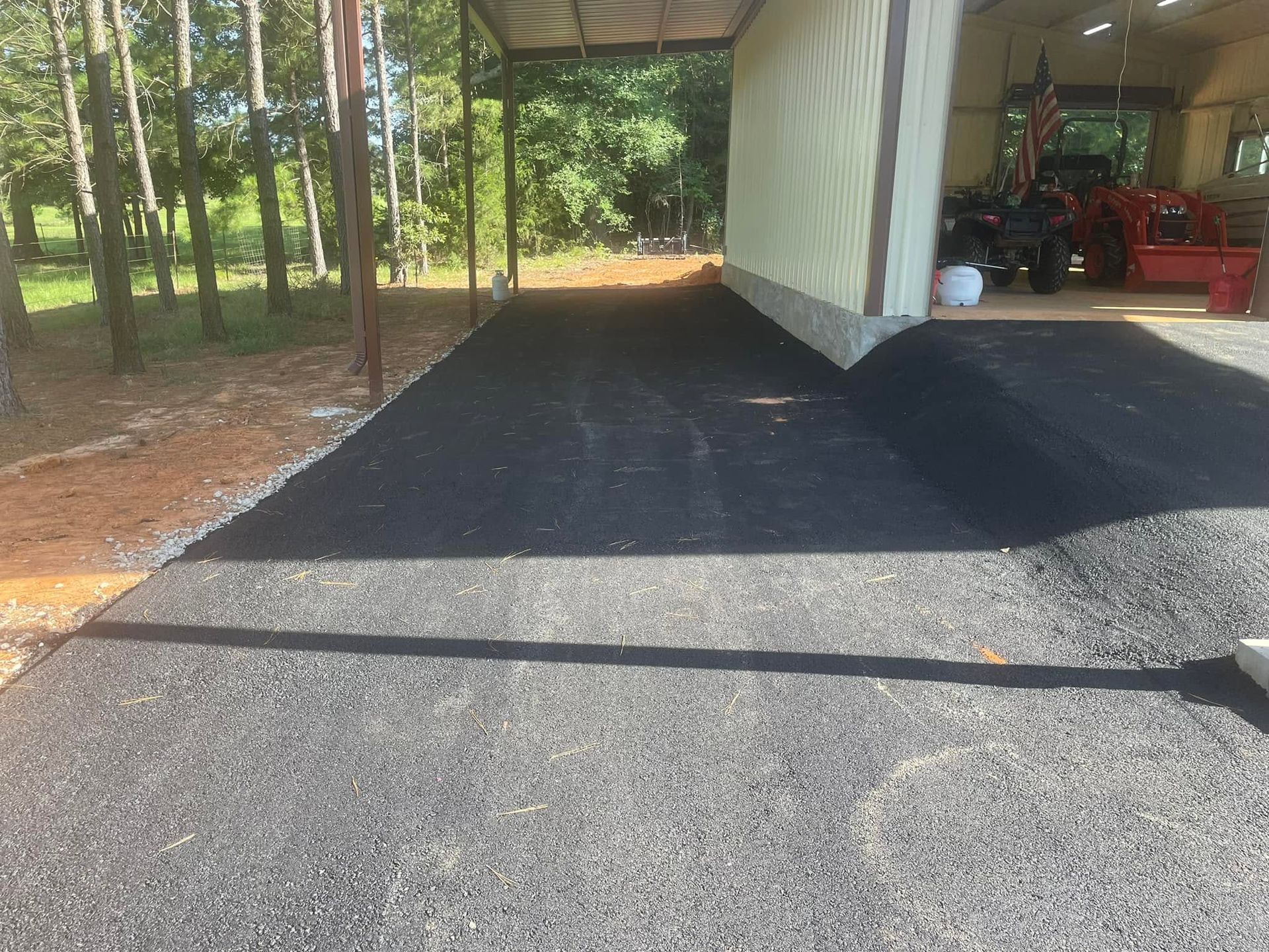 Gravel driveway beside a carport with fresh black asphalt patching and a covered storage area.