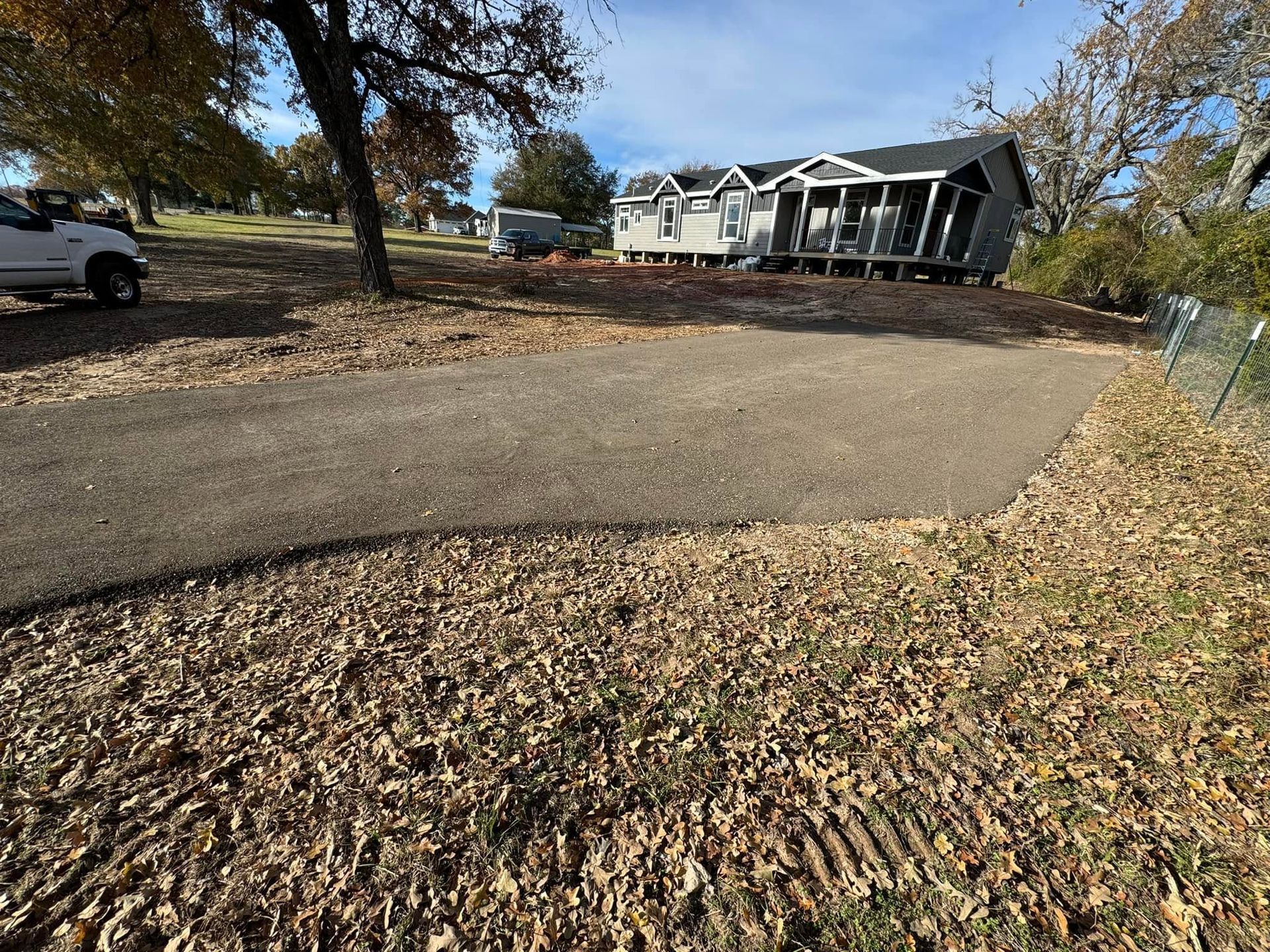 Leaf-covered driveway curving past trees toward a white house on a sunny autumn day