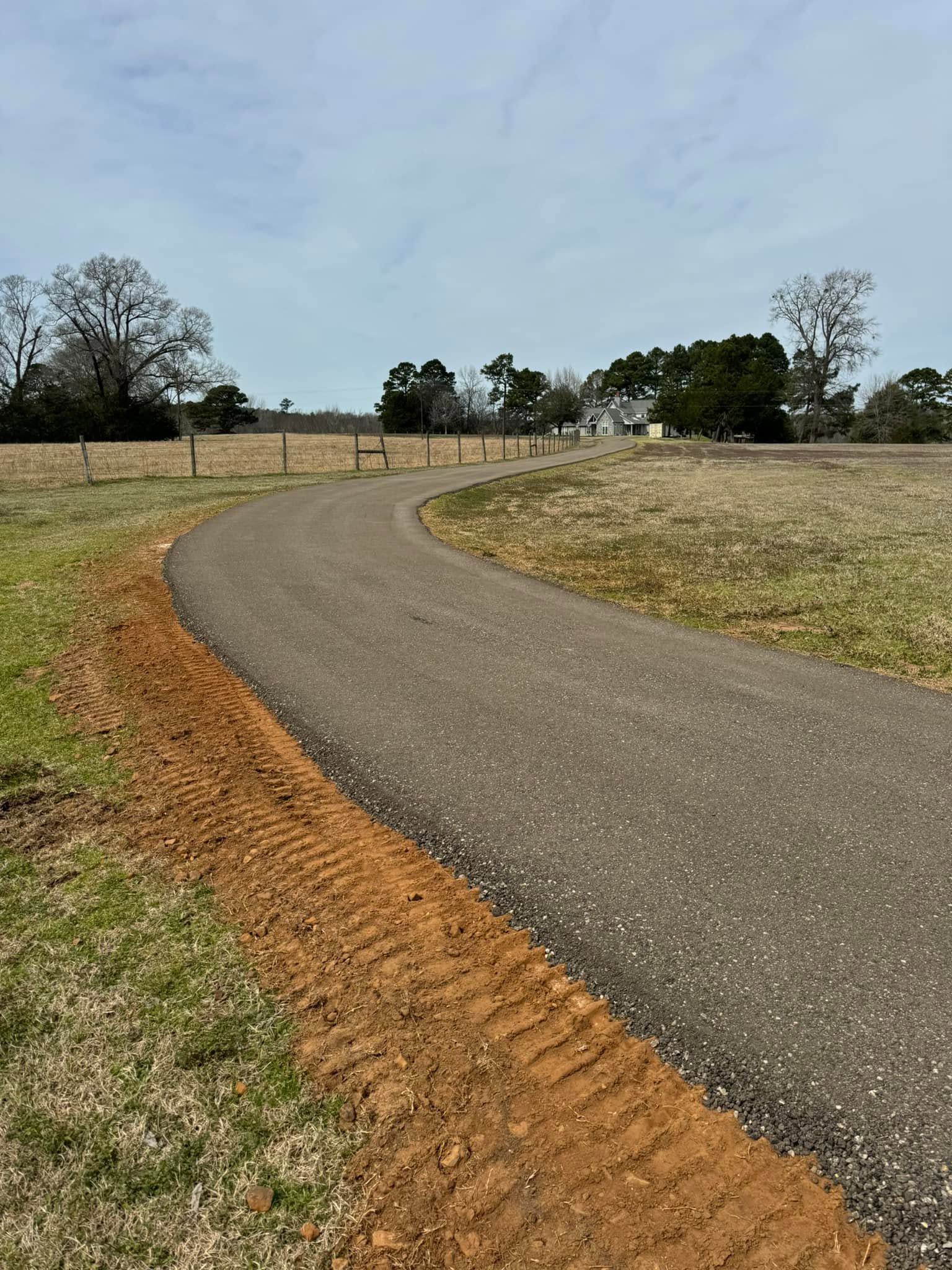 Curving paved path beside grassy fields under a partly cloudy sky