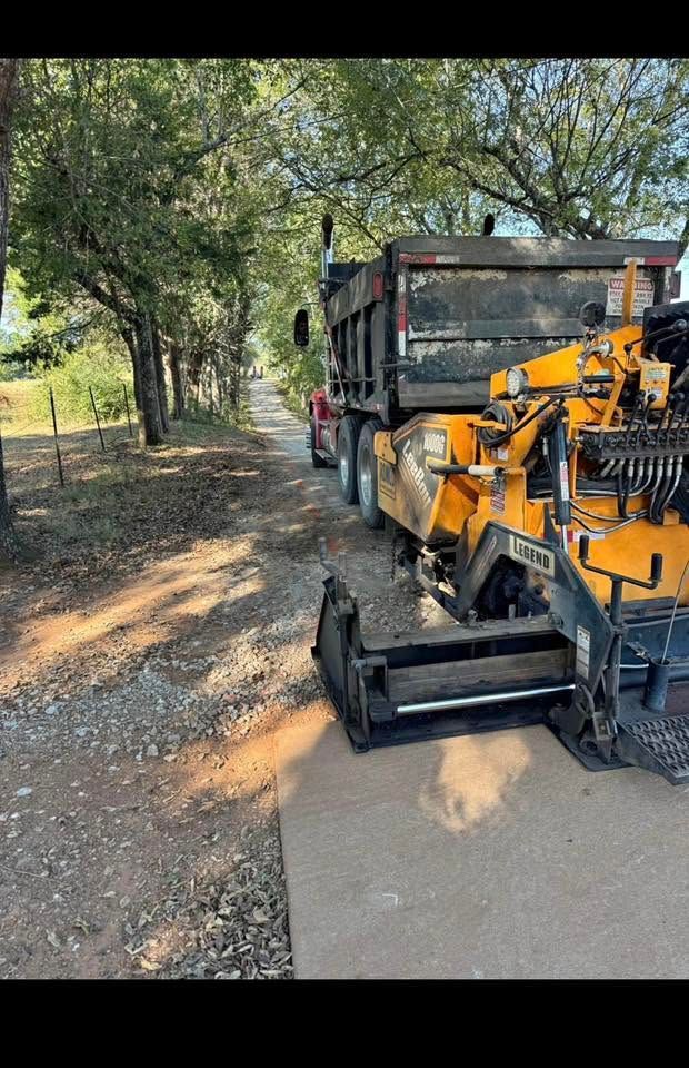 Orange construction machine and dump truck parked on a dirt roadside under trees