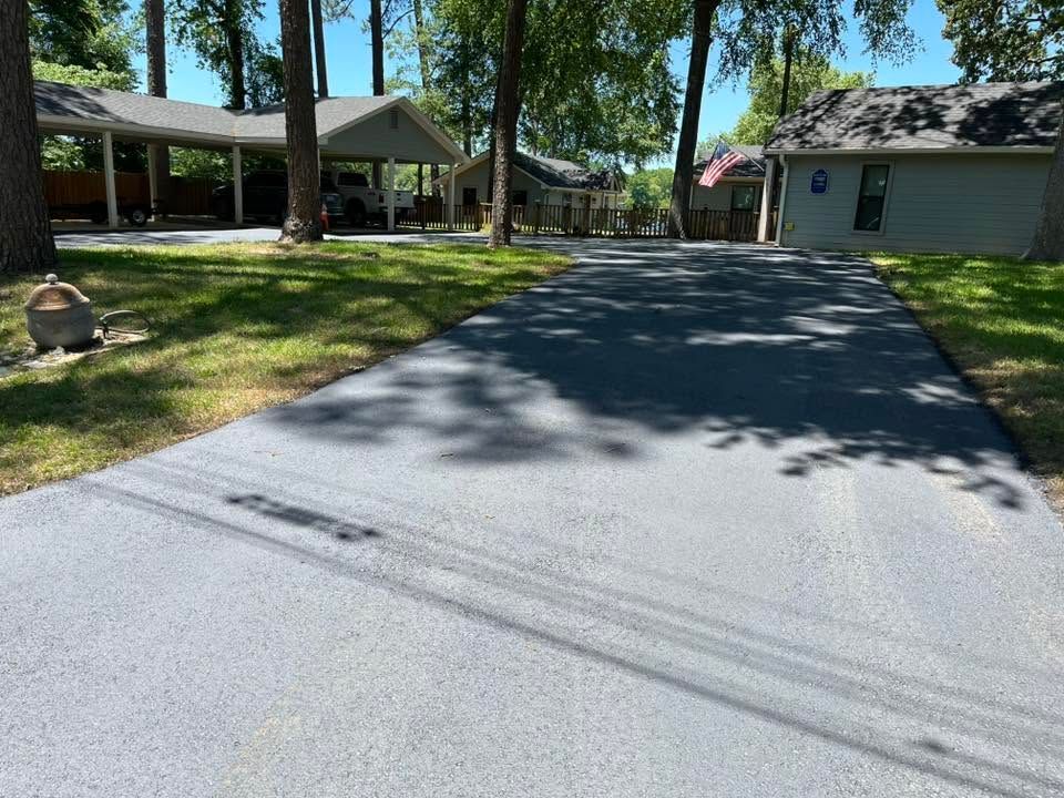 Shaded residential driveway leading to a single-story house with trees and lawn on a sunny day