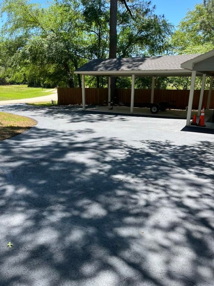 Covered driveway beside a house with trees and bright sunlight casting shadows on the pavement