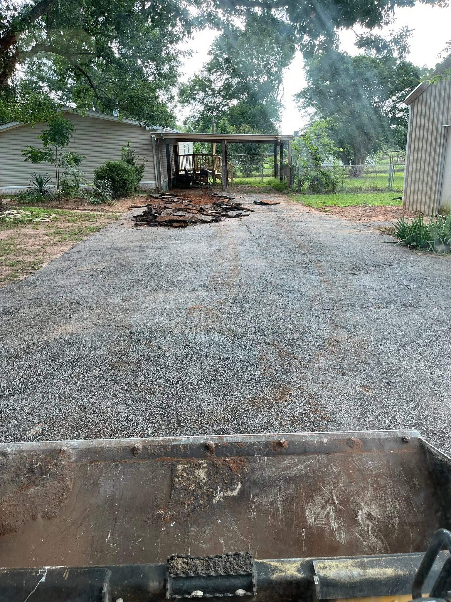 Gravel driveway leading to a small shed and trees, viewed from inside a vehicle.