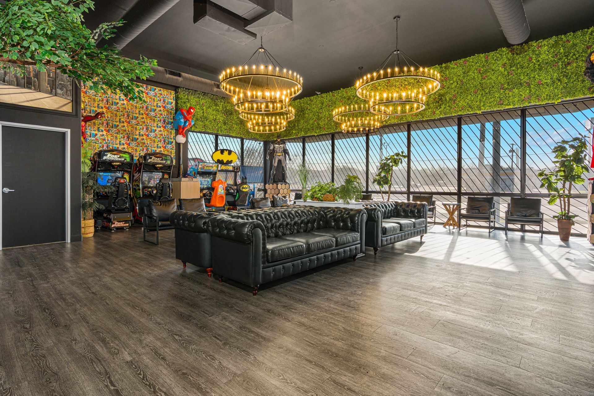 Modern lounge with green sofas, chandeliers, and floor-to-ceiling windows overlooking a sunny outdoor view