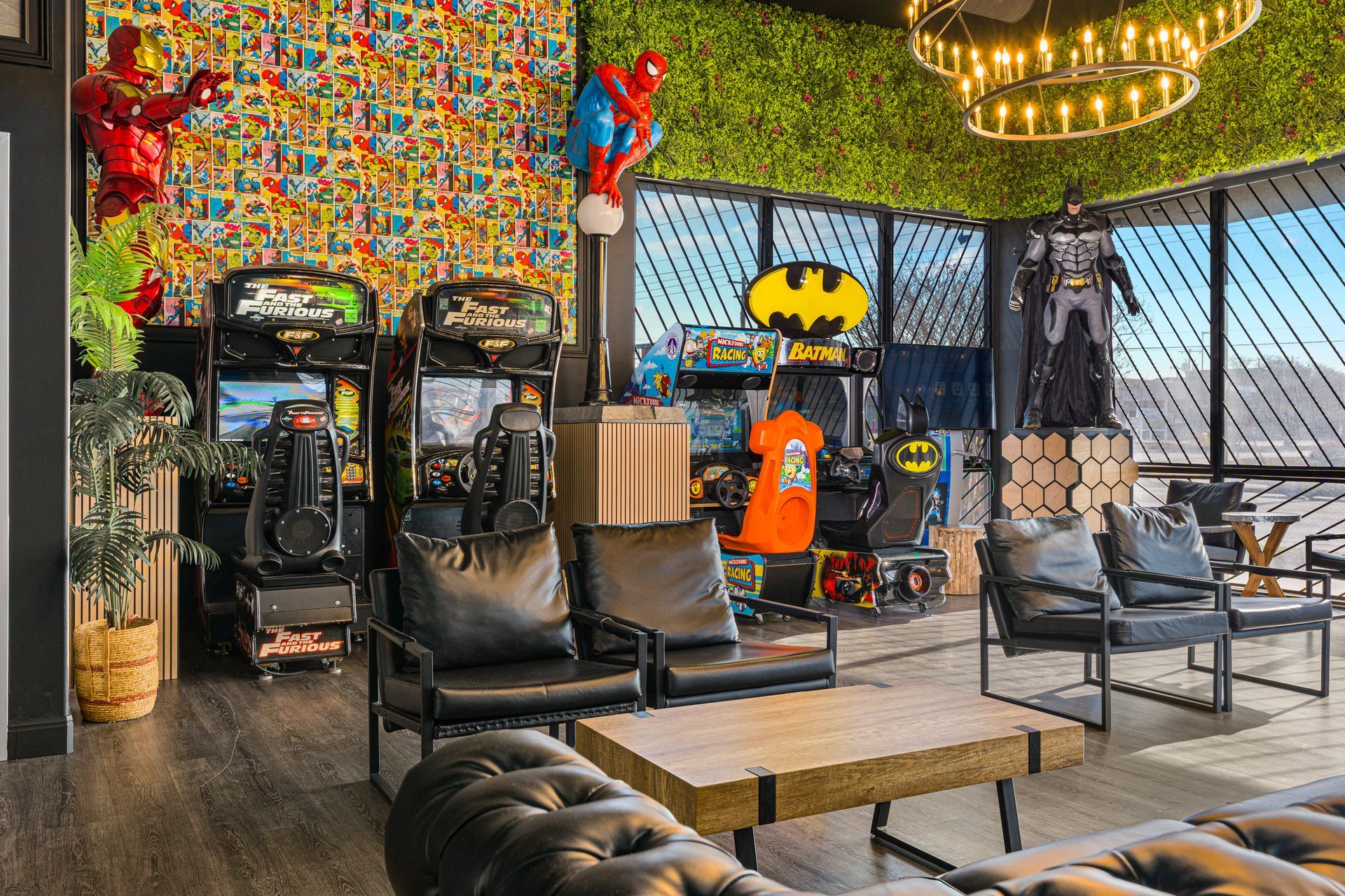 Eclectic lounge with black chairs, arcade games, Batman decor, and colorful mosaic walls