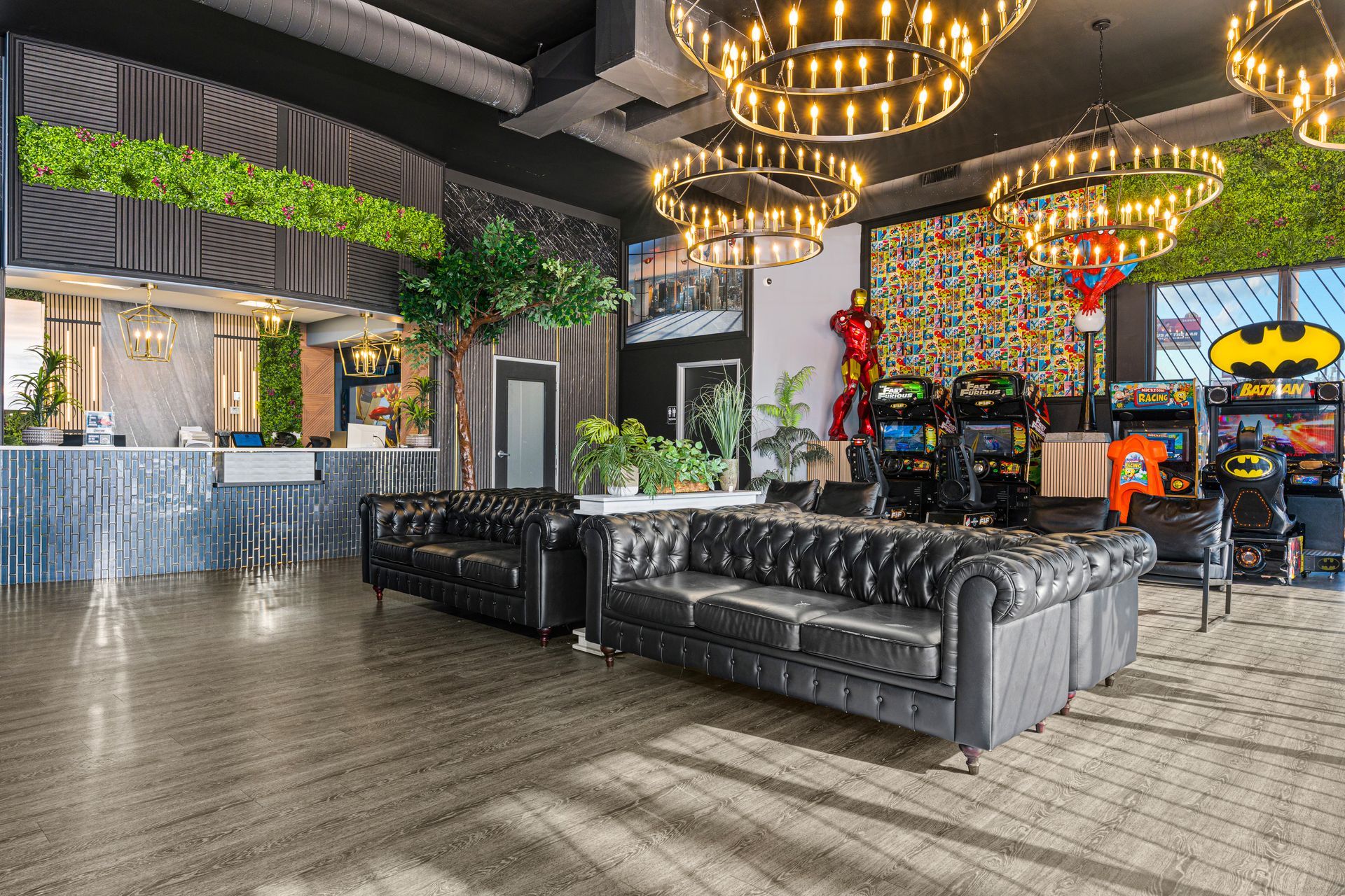 Modern lounge with black leather sofas, chandeliers, and colorful arcade machines under a high ceiling
