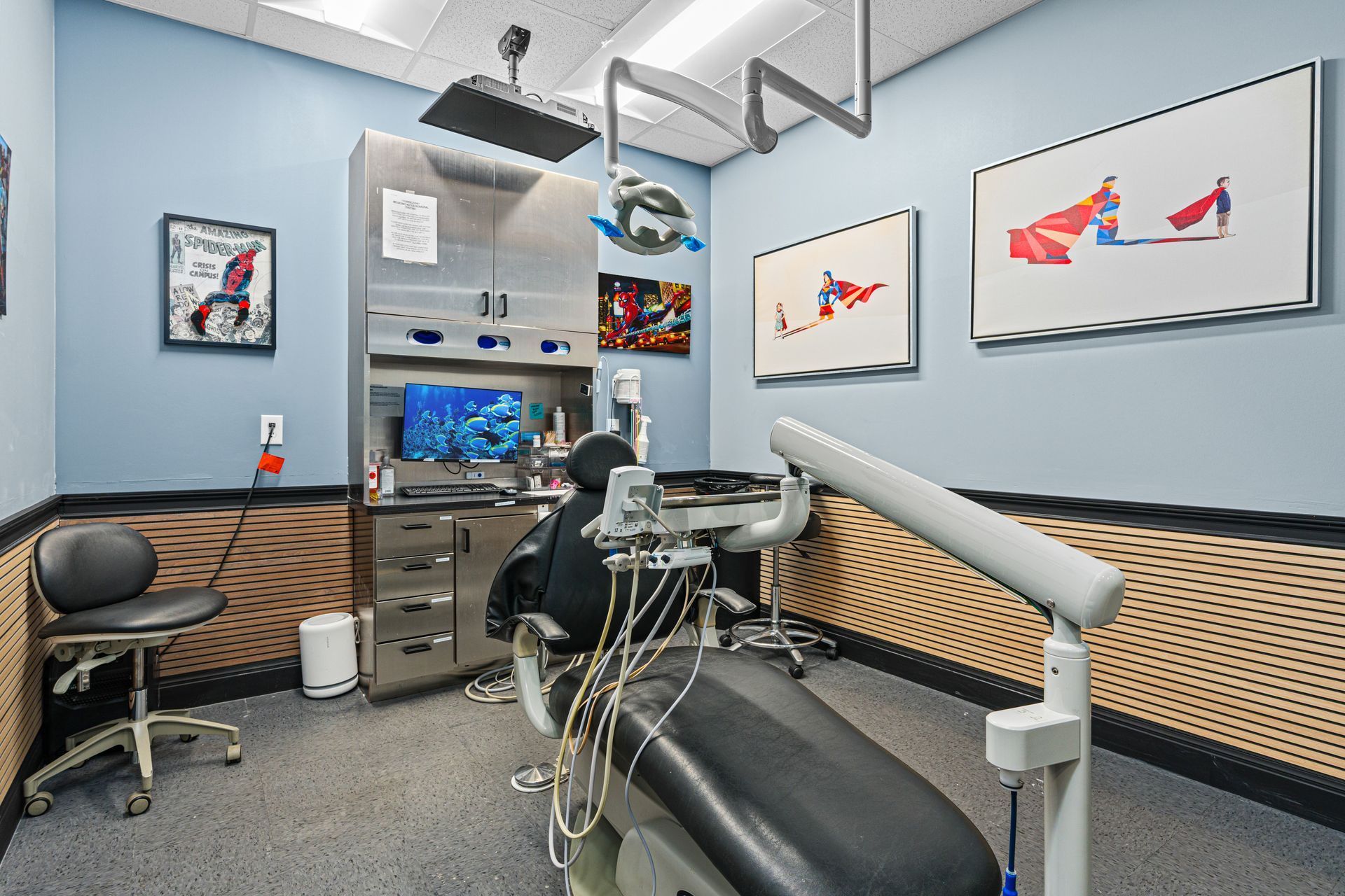 Empty dental exam room with chair, tools, and framed fish artwork on blue-gray walls
