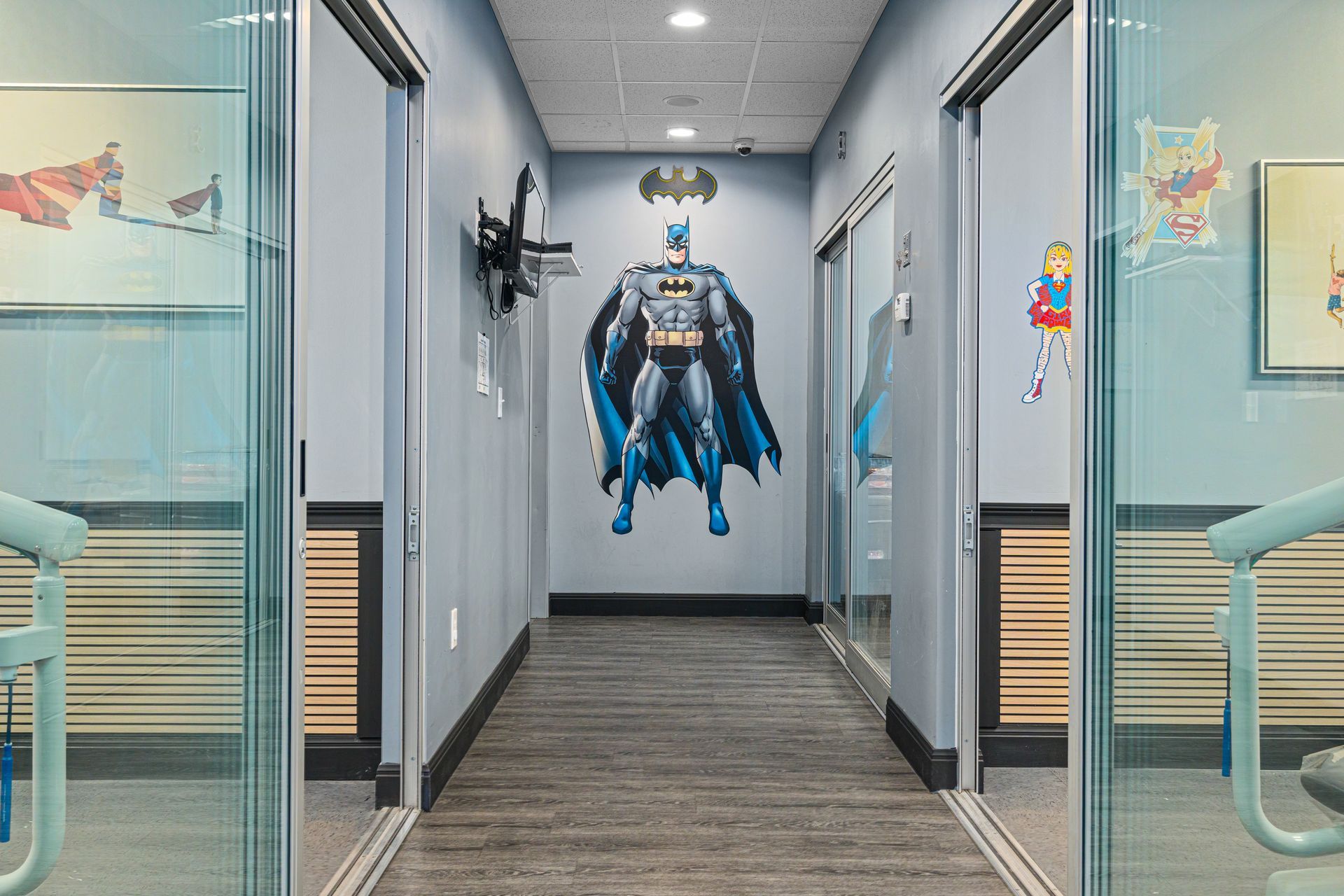 Hallway with a large Batman cutout at the far end, blue walls, and glass office doors