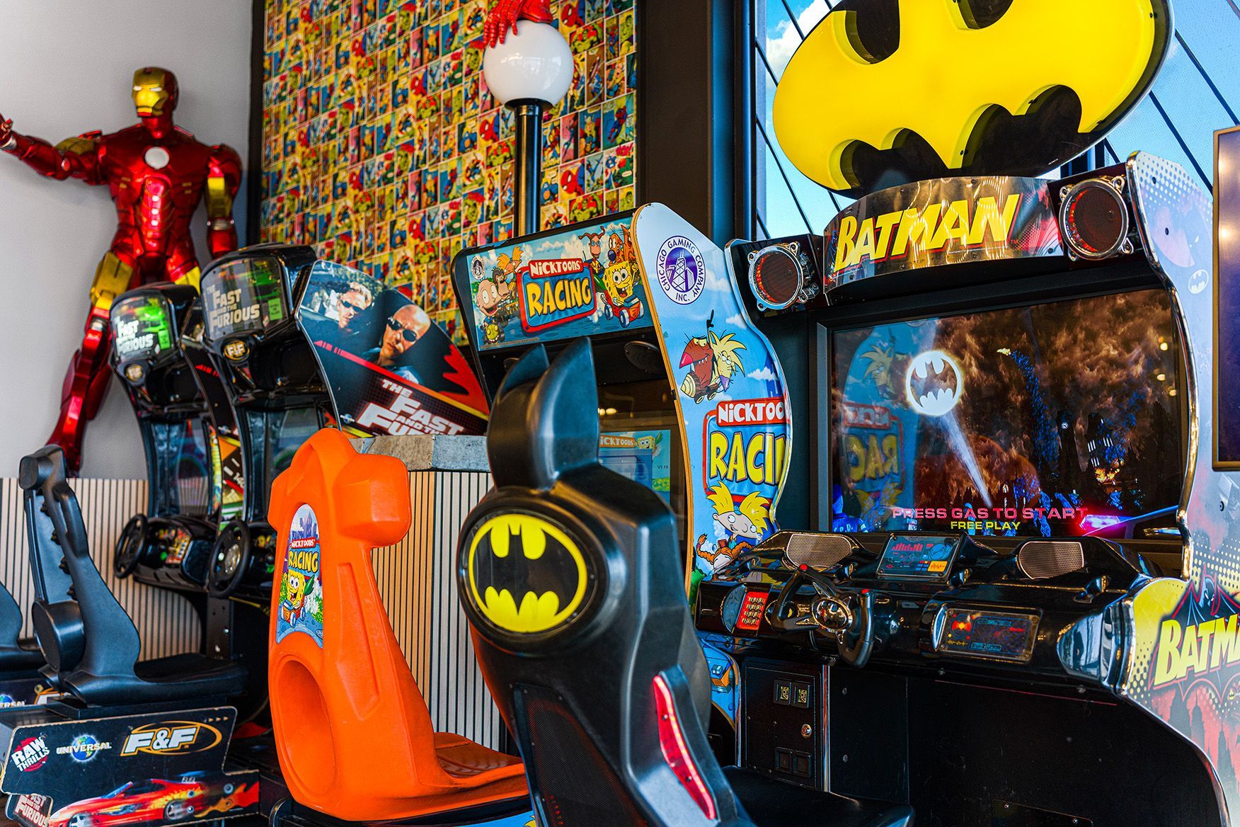 Batman-themed arcade room with game cabinets, red superhero figure, and colorful comic-style decor