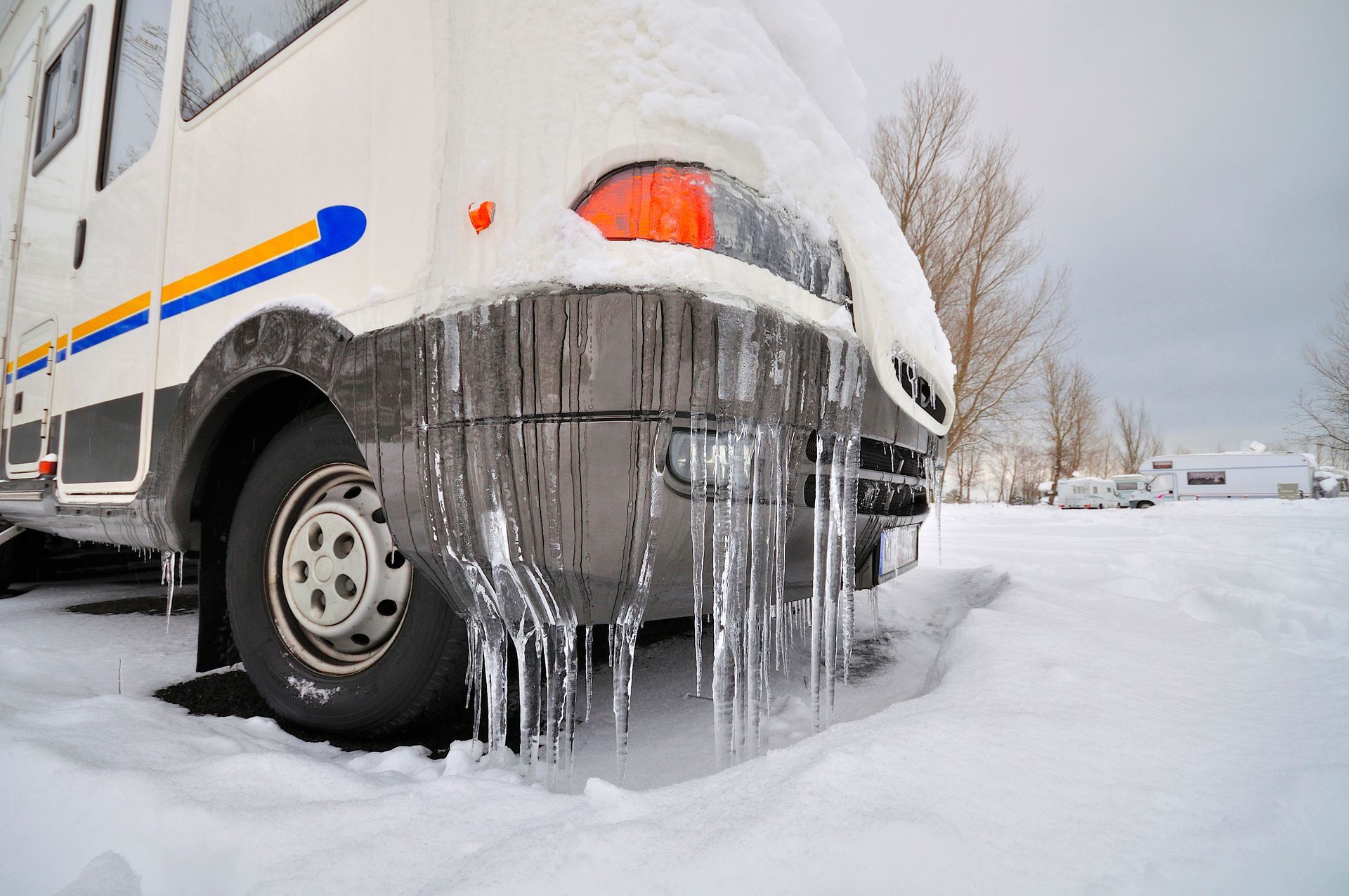 RV covered in snow and icicles in a winter campsite.
