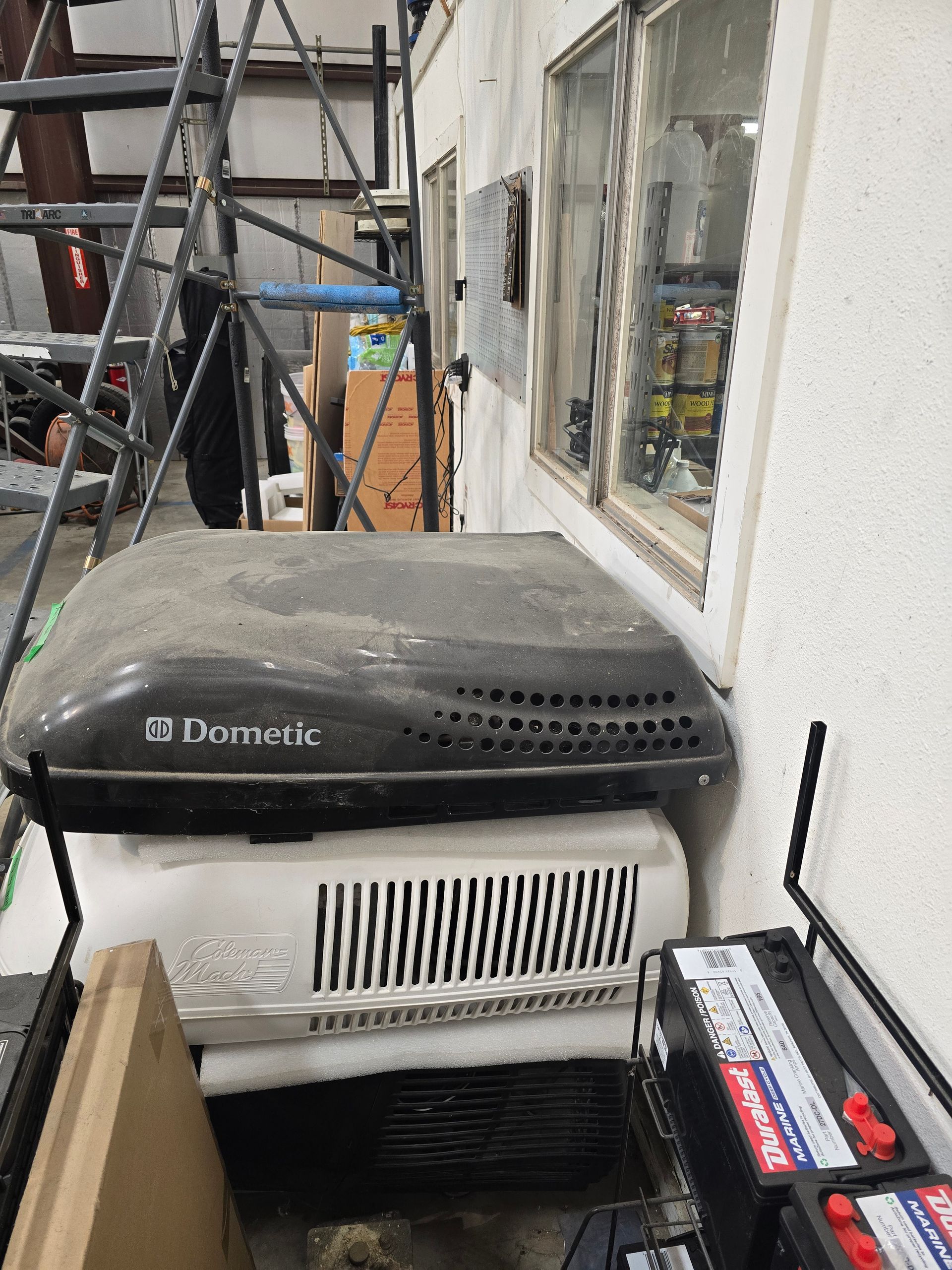 Black-and-white portable heater amid construction tools beside a window on a rooftop/utility area