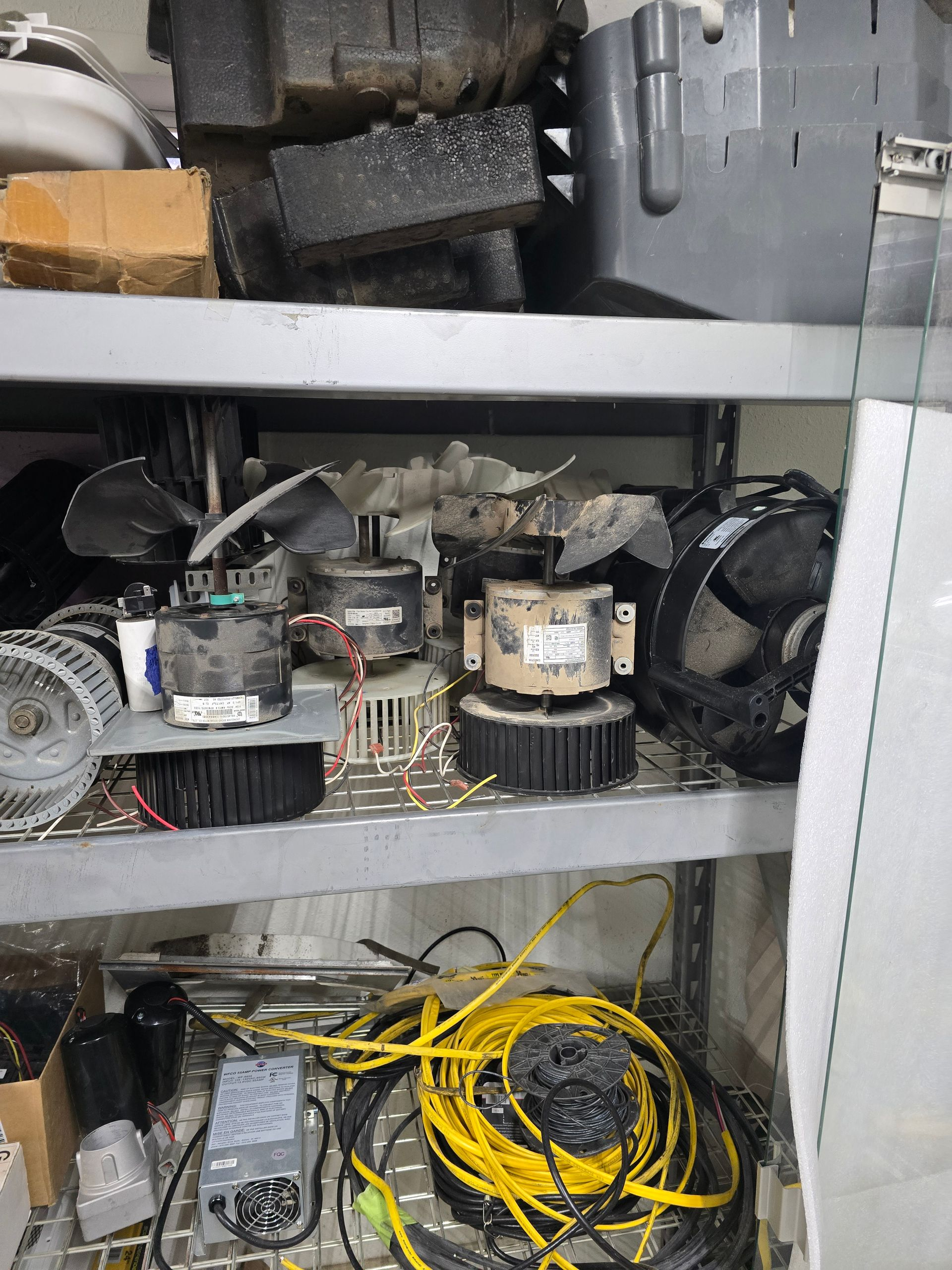 Shelved garage parts, including motors, a fan, and tangled yellow and black cords.
