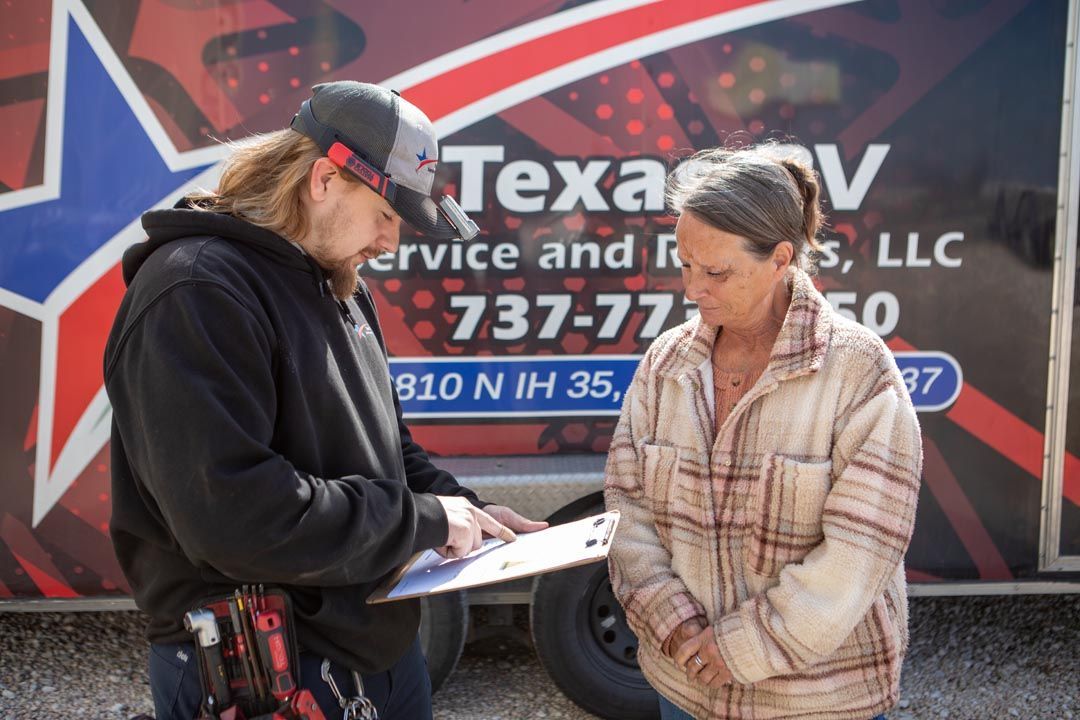 Man in cap shows clipboard to woman near a trailer with 