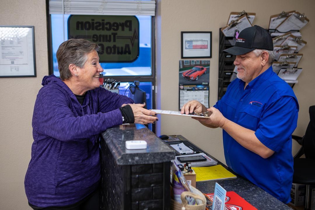 Woman handing papers to a man at a business counter. Man wears a blue shirt and hat; woman in purple.