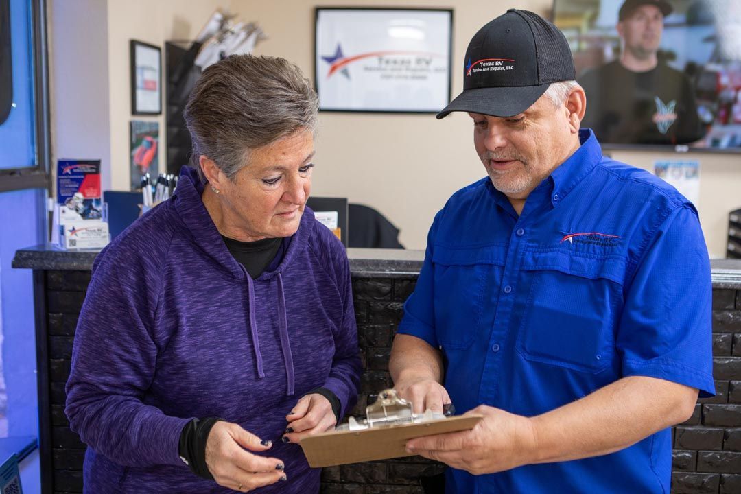 Woman and man reviewing paperwork in an office with a Texas RV sign in the background. Man wears a hat and blue shirt.